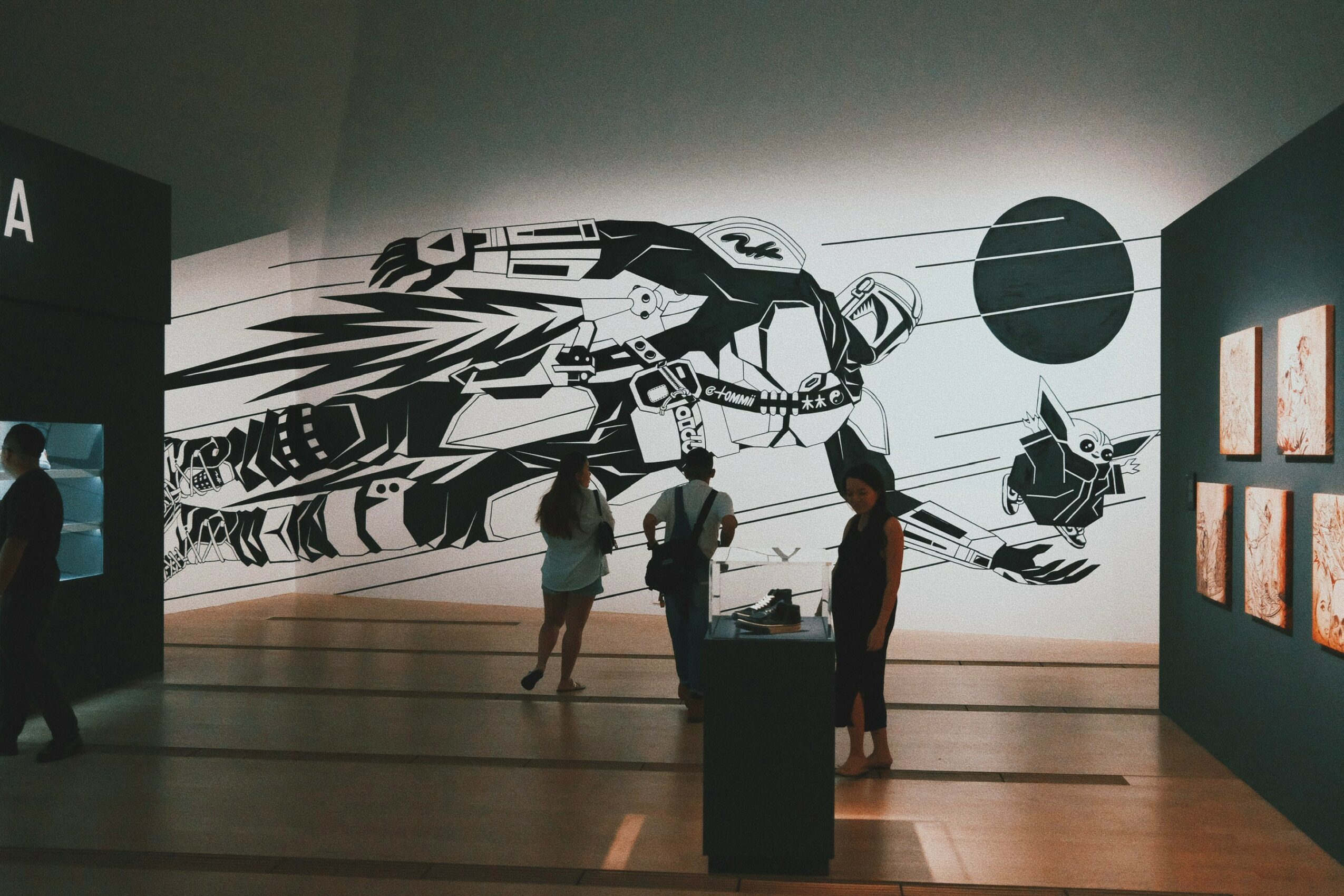 People observe a large black and white mural of a futuristic spaceship in an exhibition space.