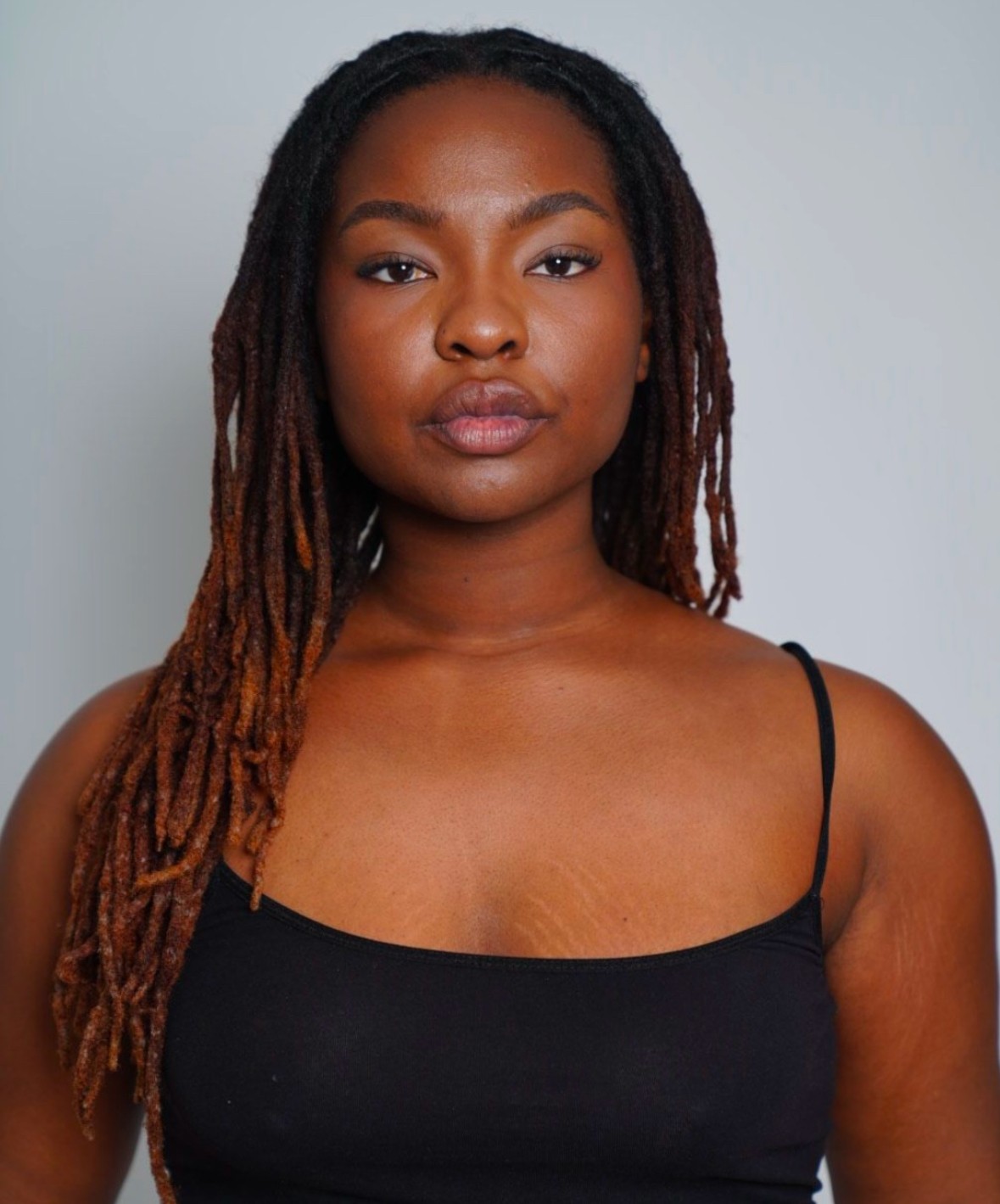 Portrait of a woman with long dreadlocks wearing a black spaghetti strap top, looking directly at the camera.