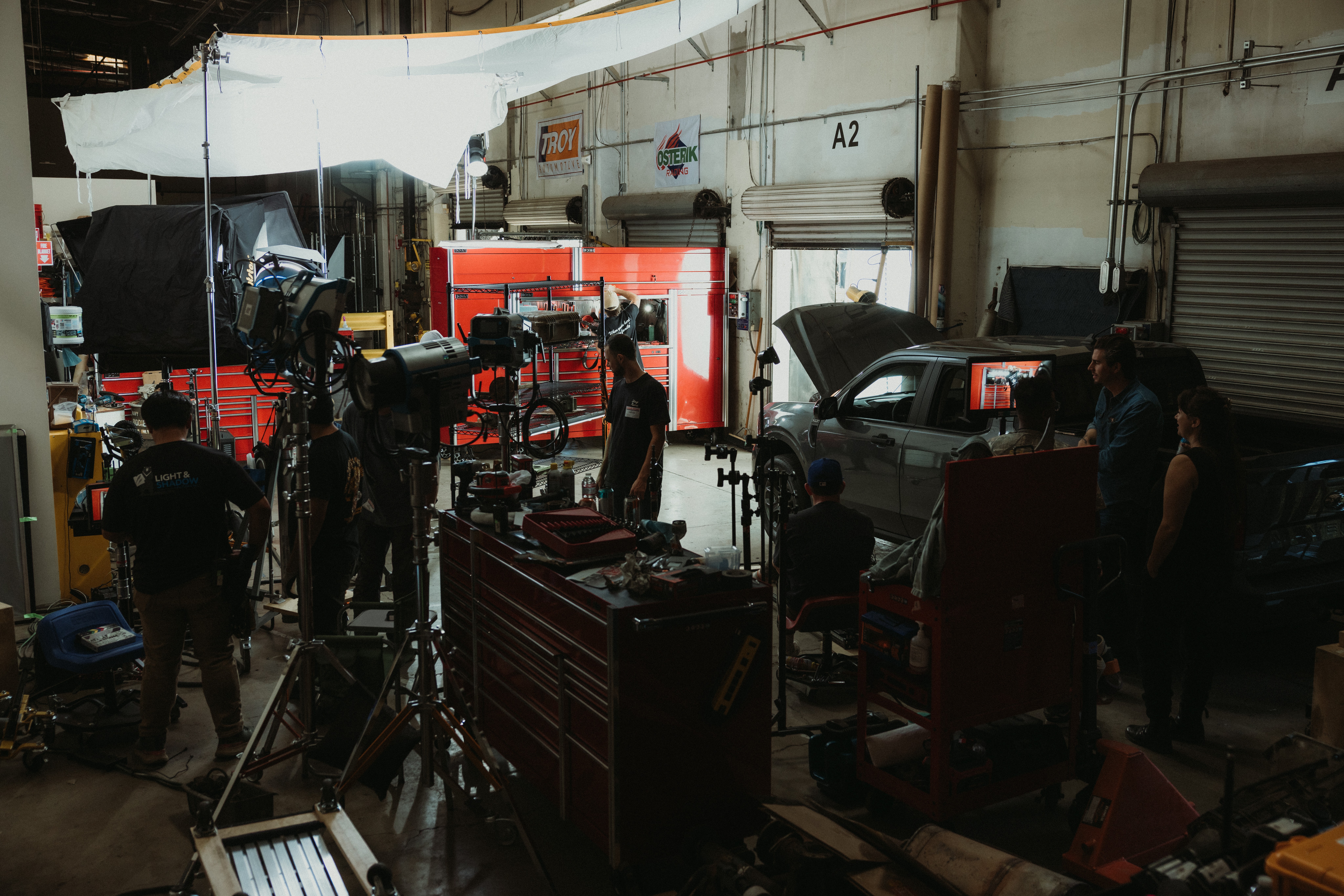 People working in an automotive repair shop with tools, equipment, and a car with an open hood.