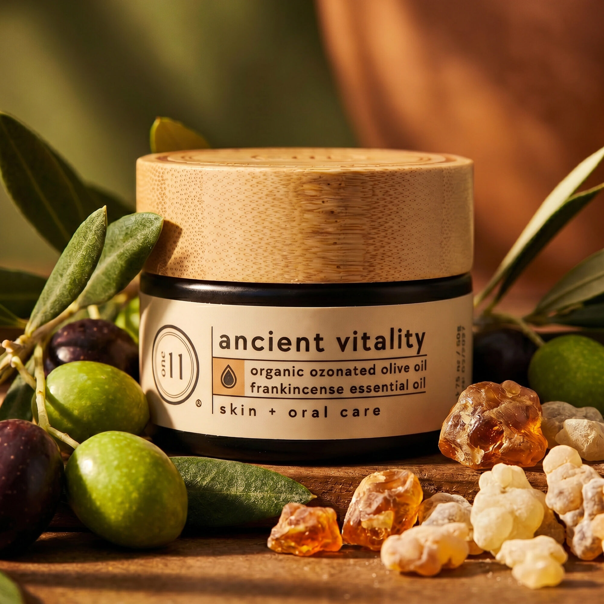 Jar of ancient vitality skincare with olive oil surrounded by olives and stones, on a wooden surface.