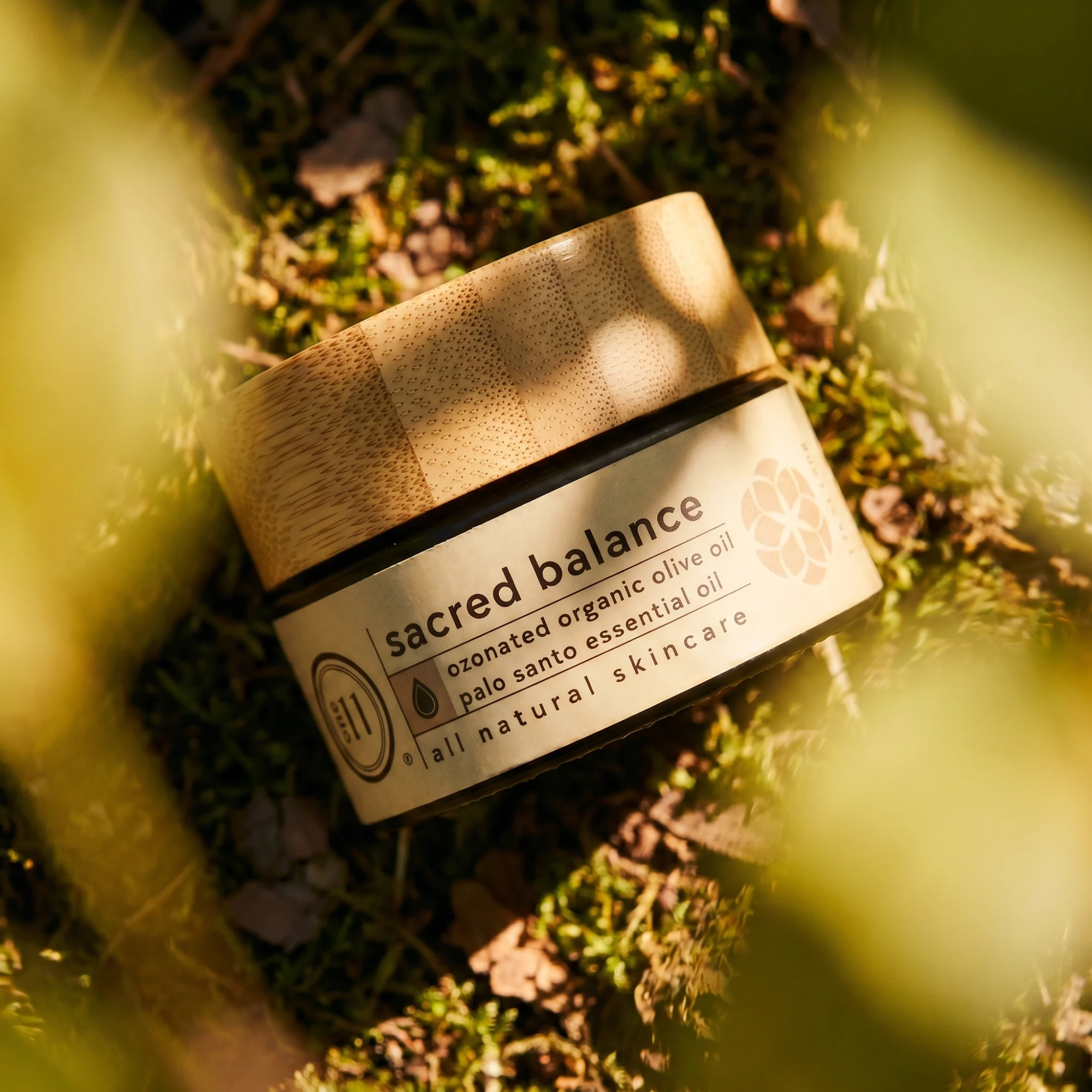 A small jar labeled 'Sacred Balance' lies on grass surrounded by blurred green leaves, with sunlight filtering through. Word details include organic olive oil and natural skincare. Word count: 20, confidence: 0.9
