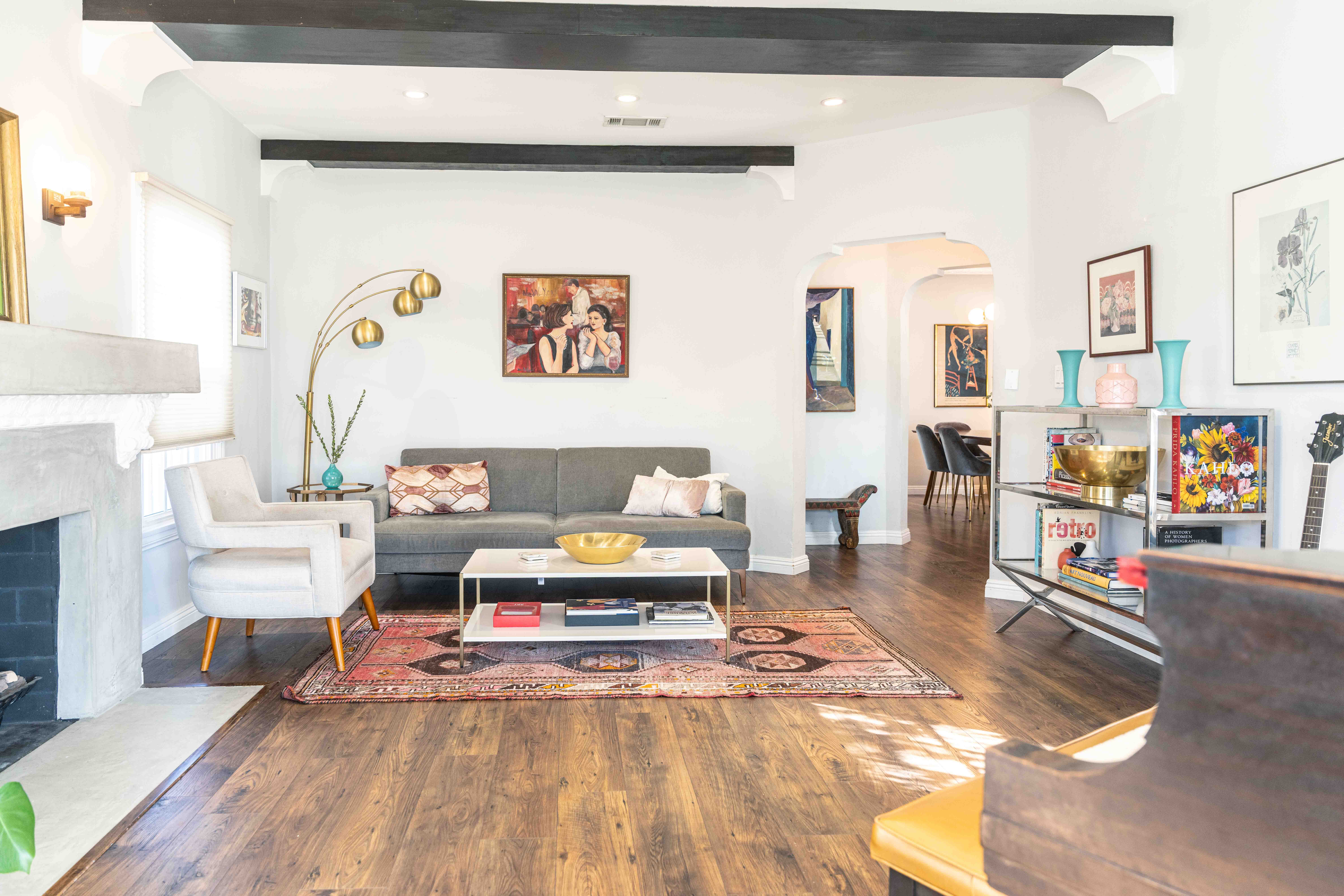 Living room with white walls, gray sofa, white armchair, wooden floor, and colorful artwork, with a fireplace on the left.