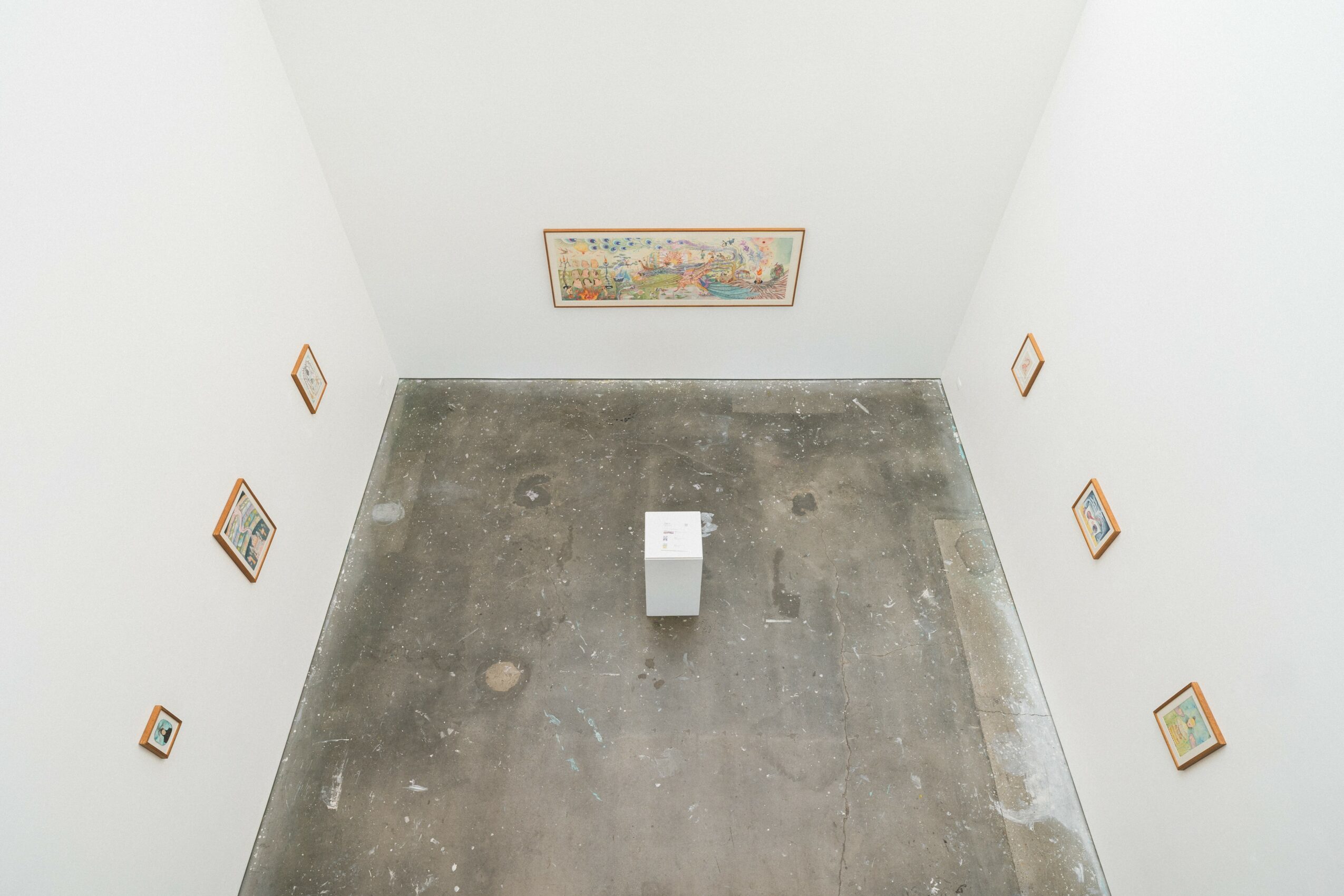 Gallery with white walls, framed artwork, and a pedestal in the center, viewed from above.