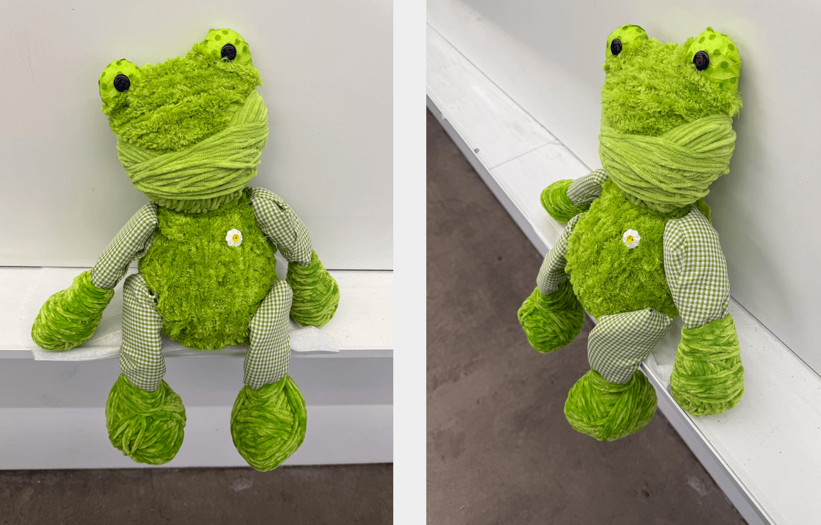 Green plush frog toy with patterned limbs, sitting against a white wall and on a gray surface, with a white button on its chest.
