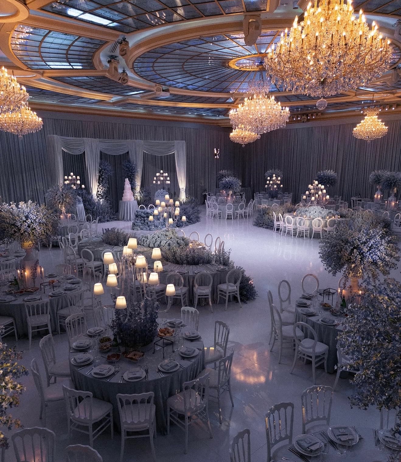 Elegant banquet hall with chandeliers, decorated tables with candles and floral arrangements, and draped curtains in the background.