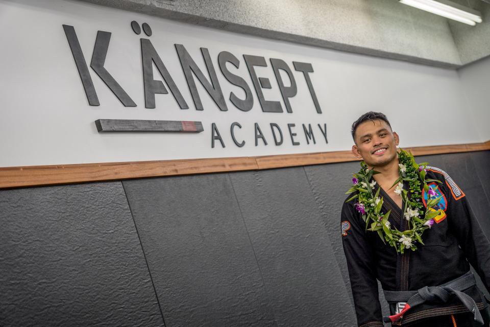 Person wearing a lei standing in front of a wall with 'KÄNSEPT ACADEMY' sign, smiling.
