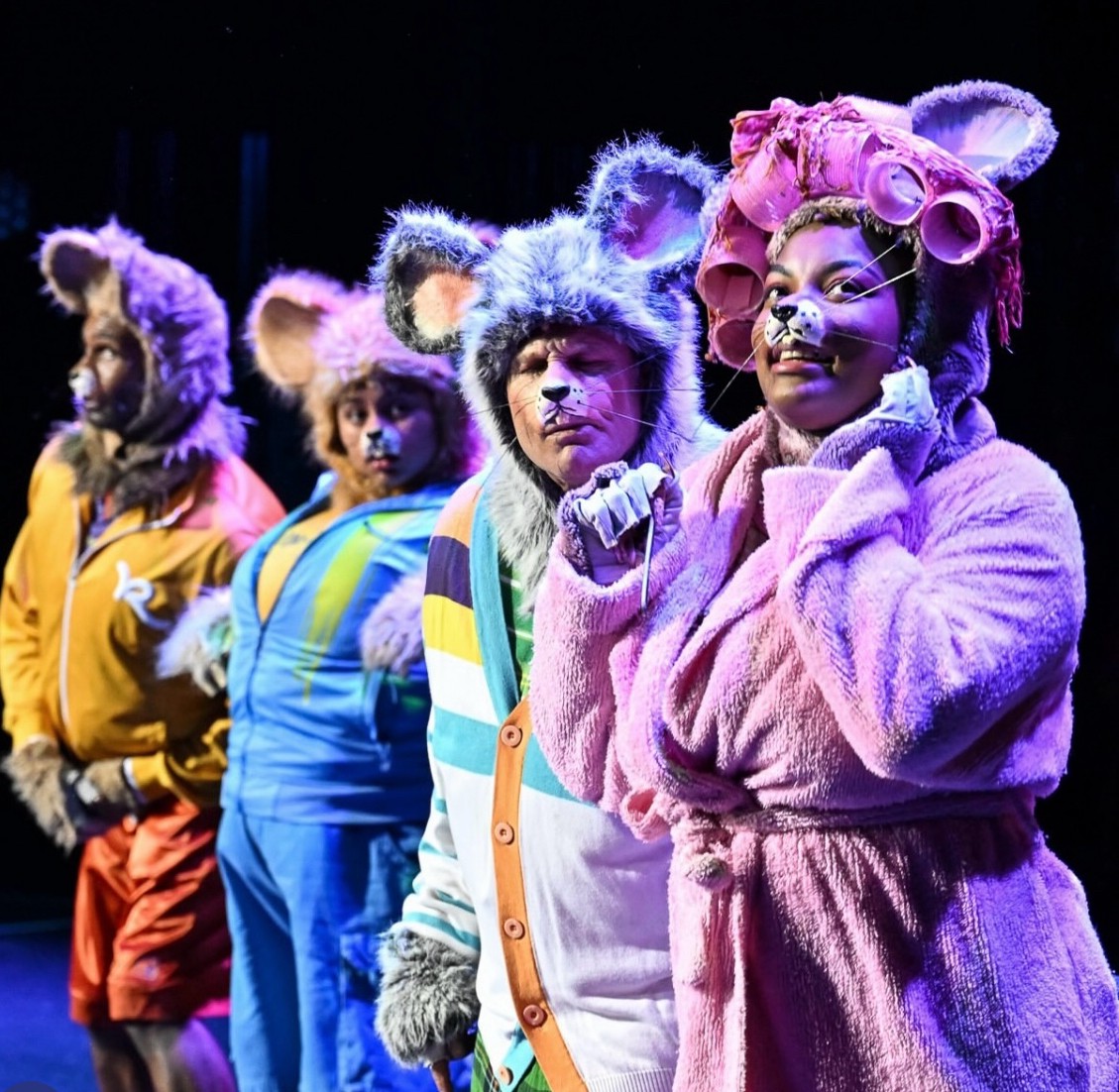 Group of children dressed as colorful animals with costumes and face paint, standing in a line on stage.