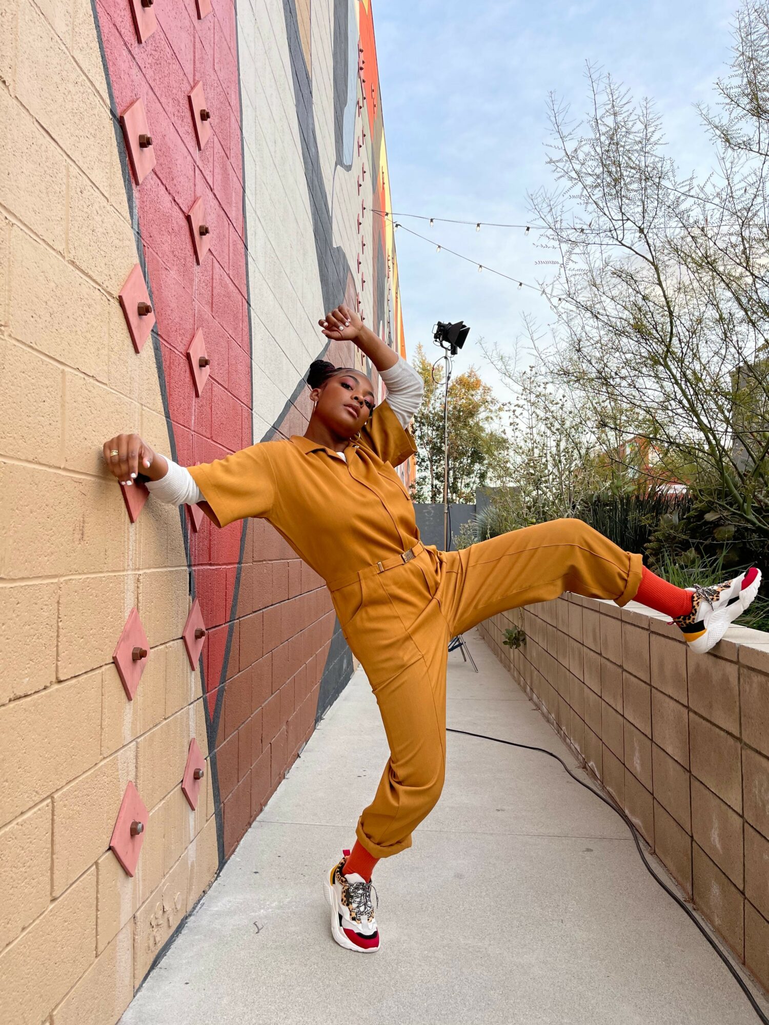 Person performing a breakdance move on sidewalk, wearing yellow pants and white sneakers, with trees and building in background.