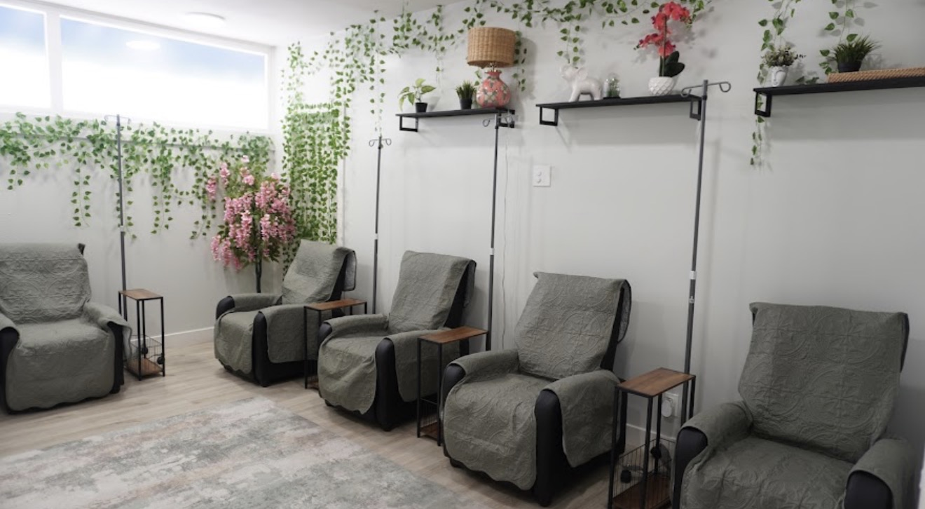 Room with five gray armchairs, small side tables, and shelves with plants and decorations, bright window on the left.