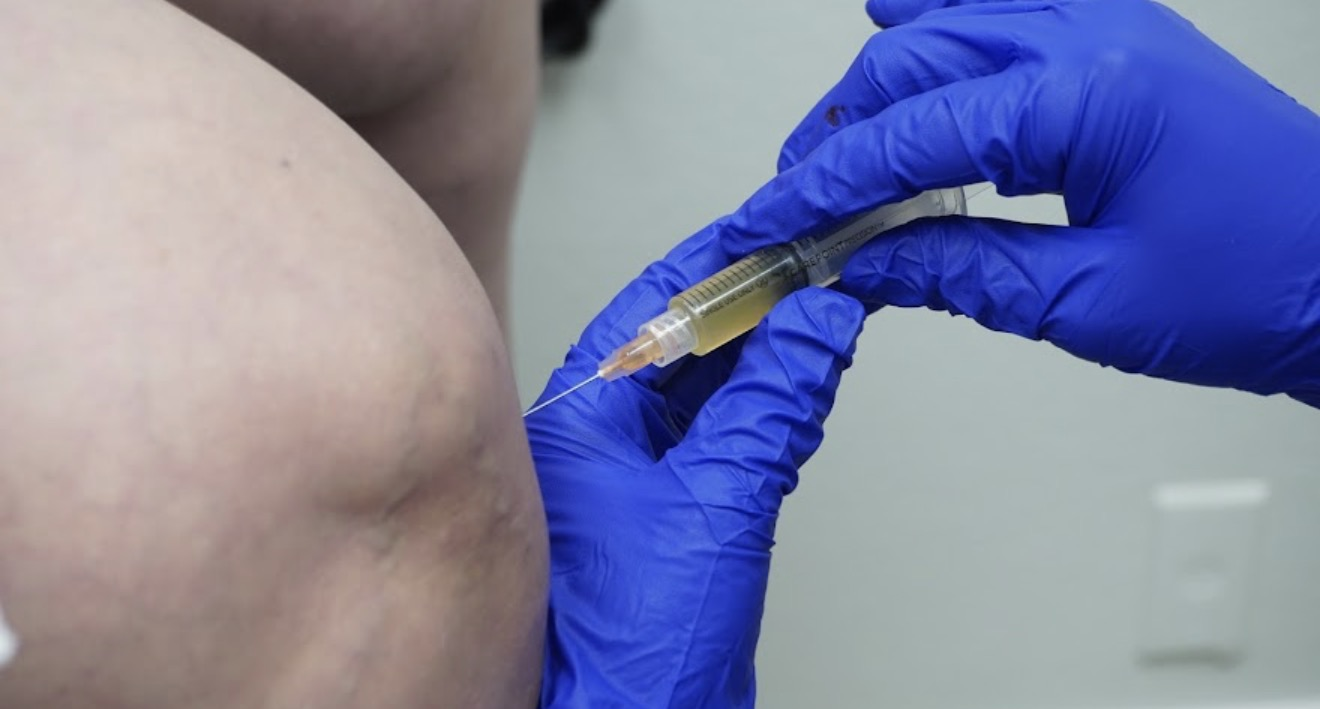 Person receiving a vaccination in upper arm, healthcare worker wearing blue gloves holding a syringe, clinical setting.