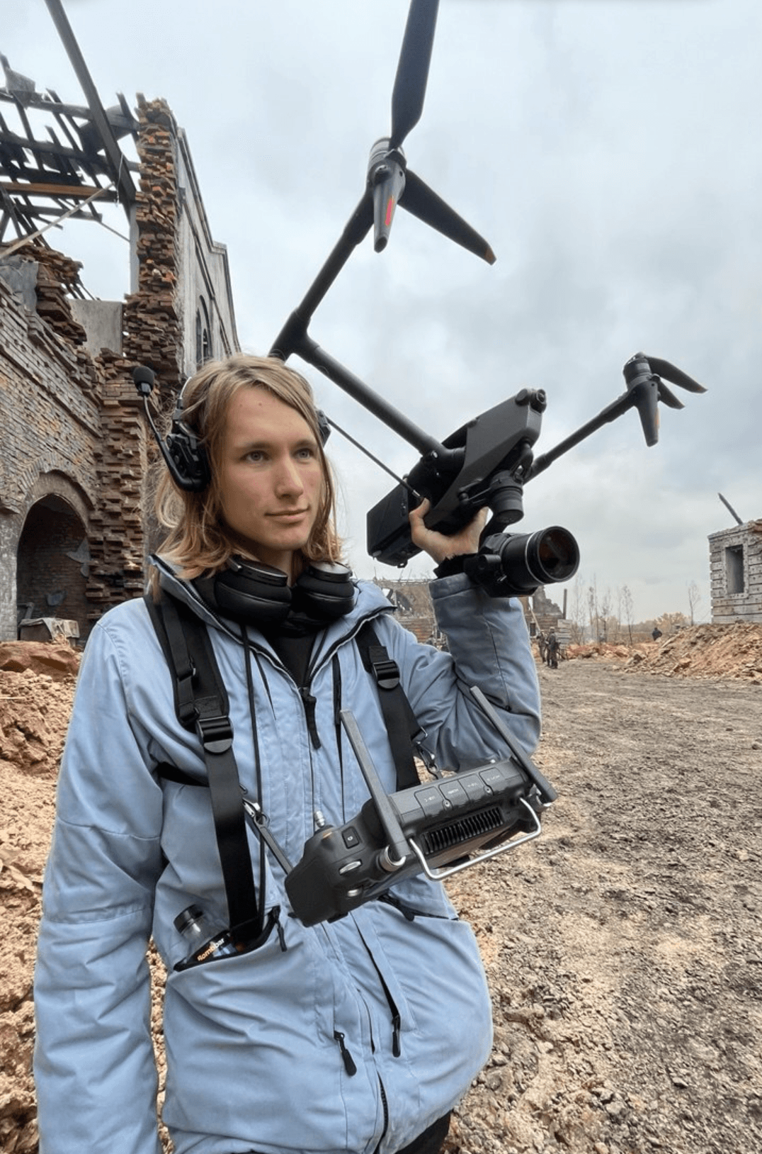 Woman holding a drone with a camera, standing outdoors in a construction area with ruins and cloudy sky