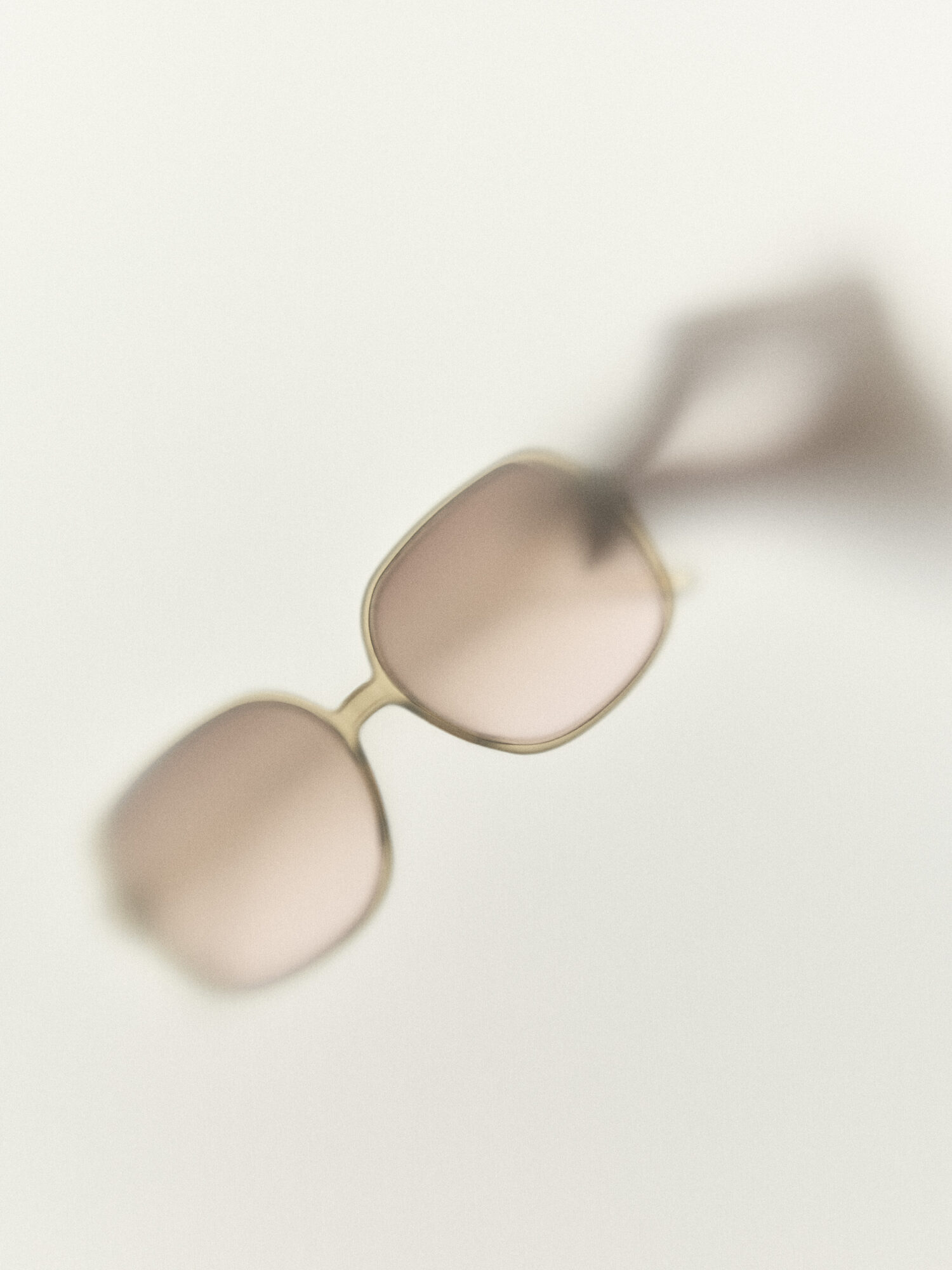 Sunglasses with light-colored frames and tinted lenses on a white surface.