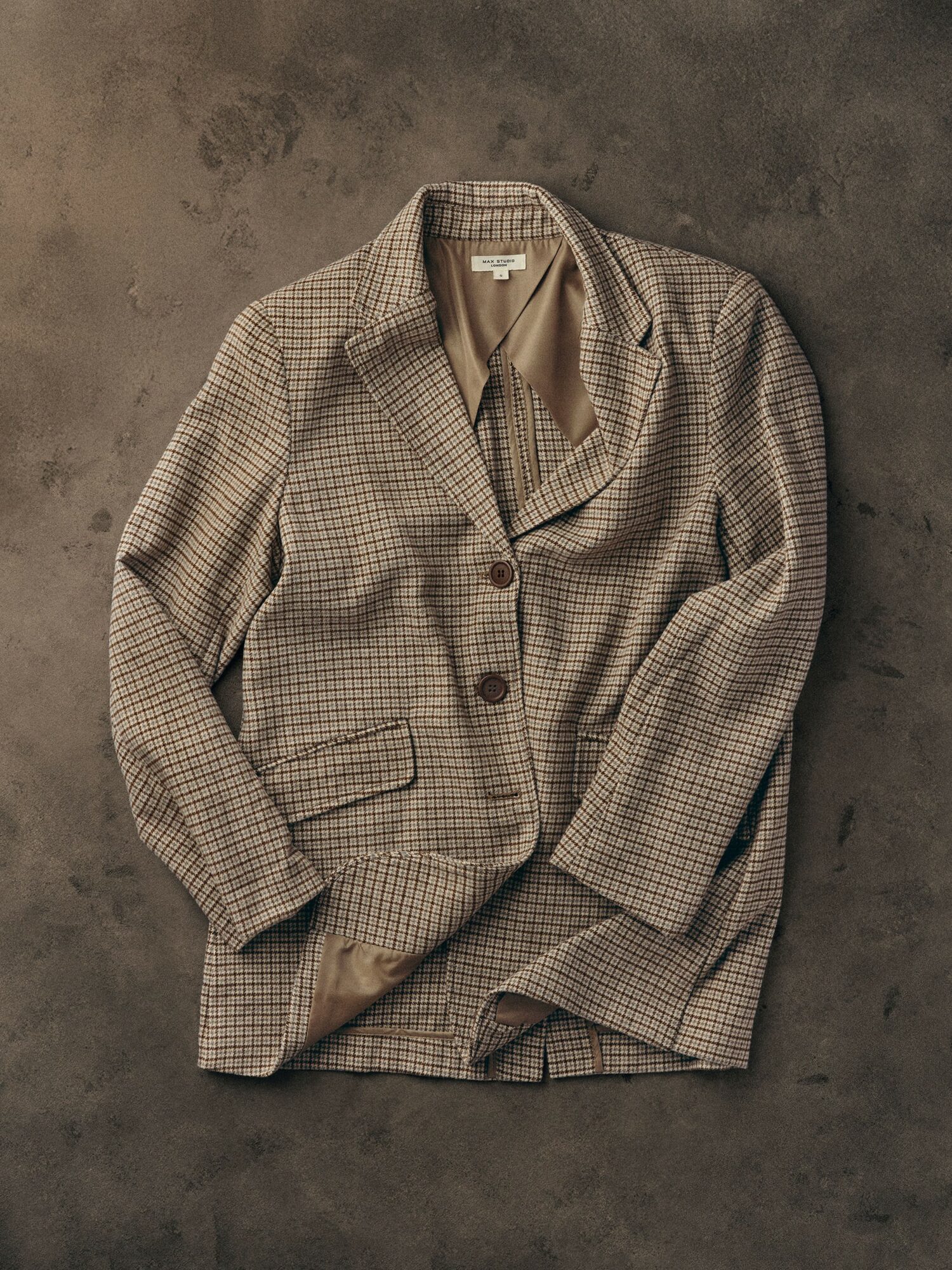 Checked blazer with lapel collar and two buttons, laid on a dark surface.