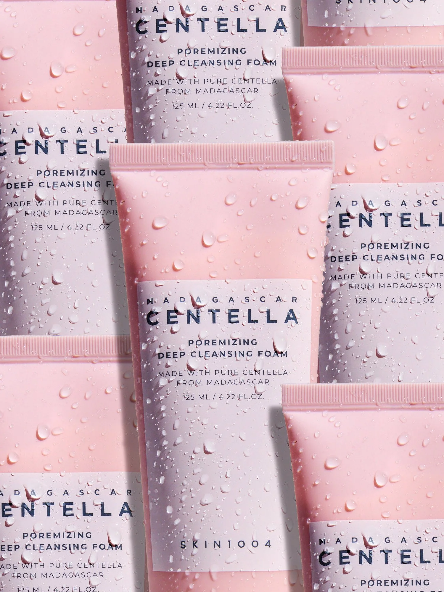 Three pink and white tubes of skincare product with water droplets, arranged on a pink background.