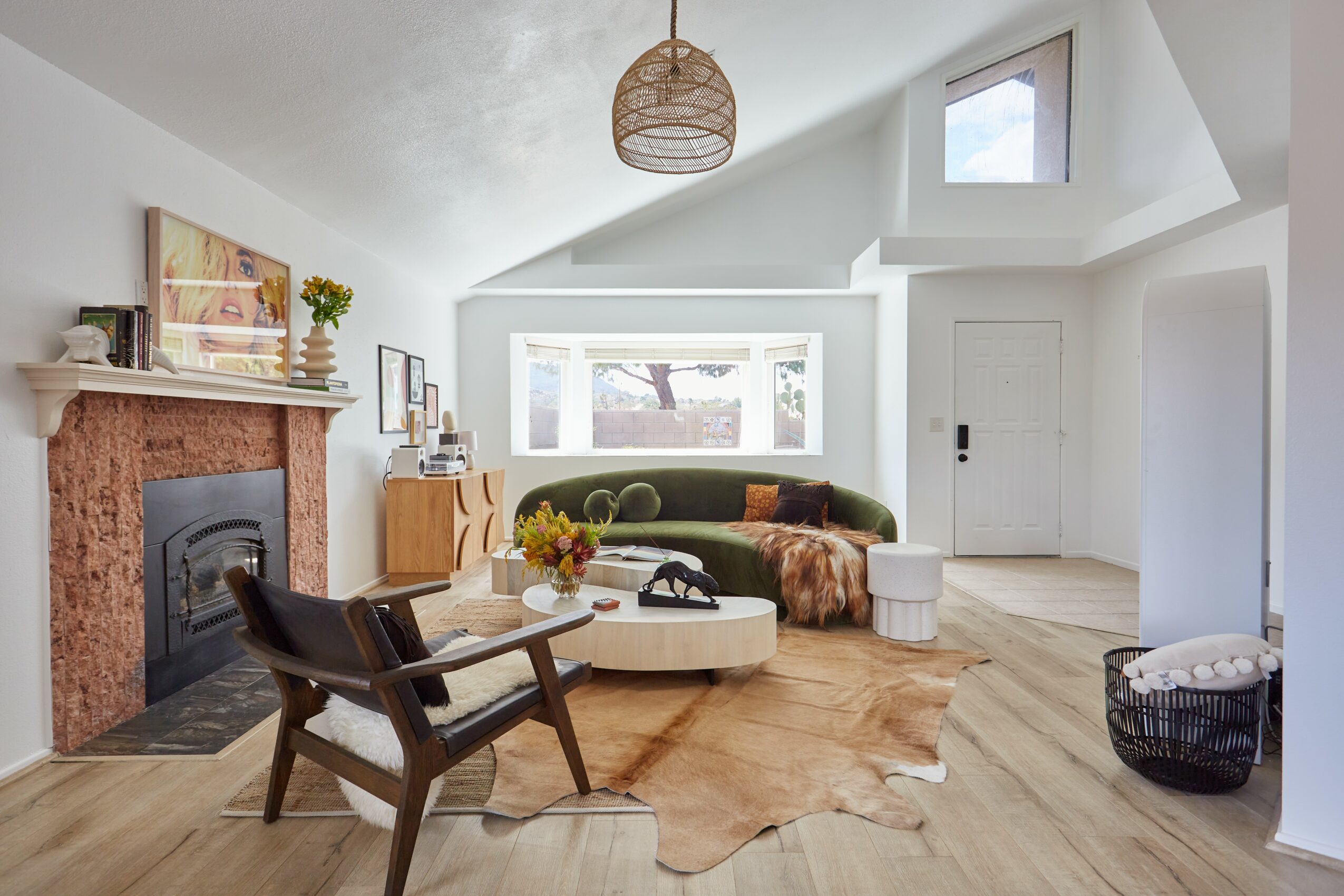 Living room with a fireplace, green sofa, wooden chair, window, and light-colored walls and flooring.