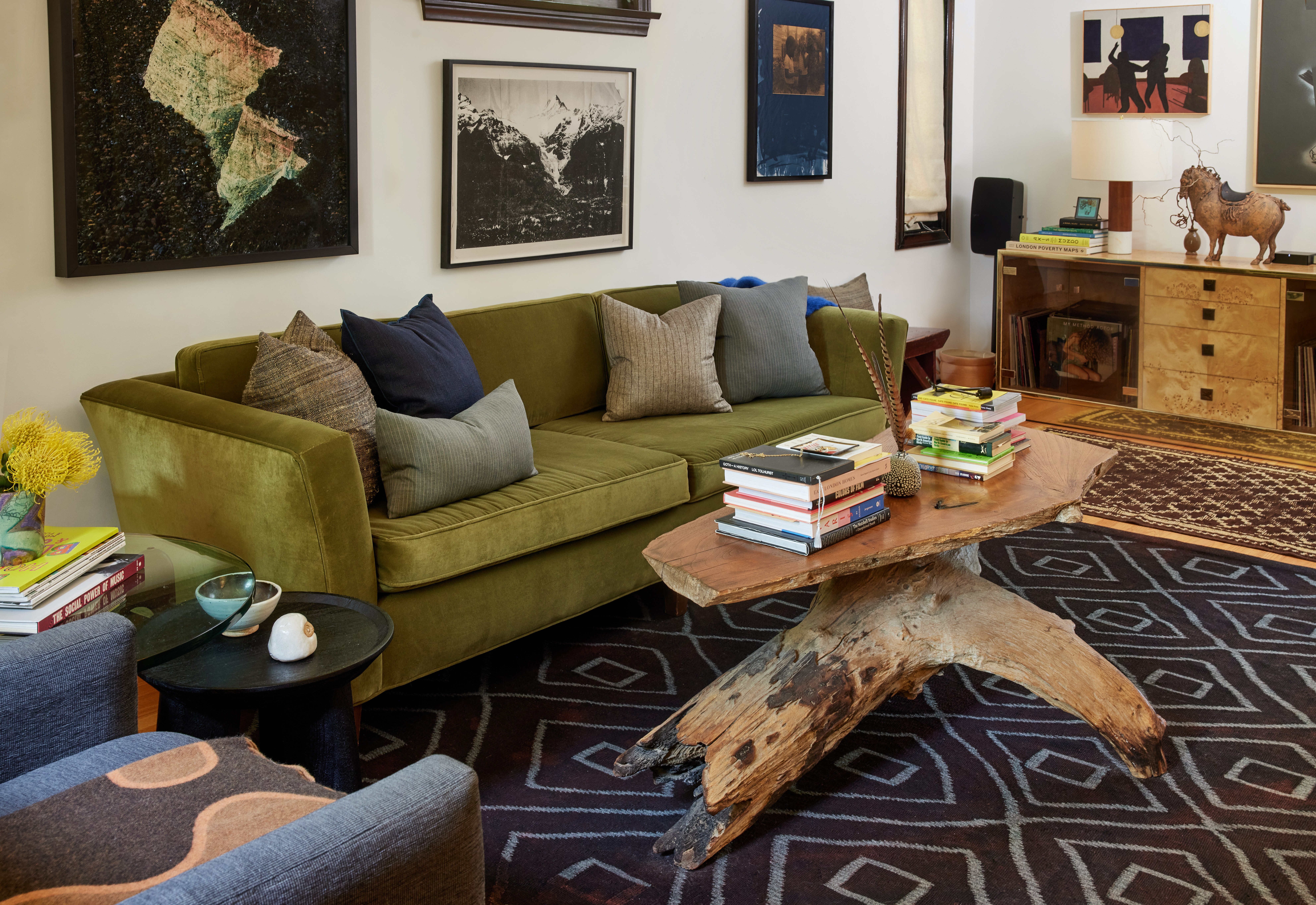 Living room with green sofa, wooden coffee table, artwork on walls, and a wooden sideboard with decorative items.