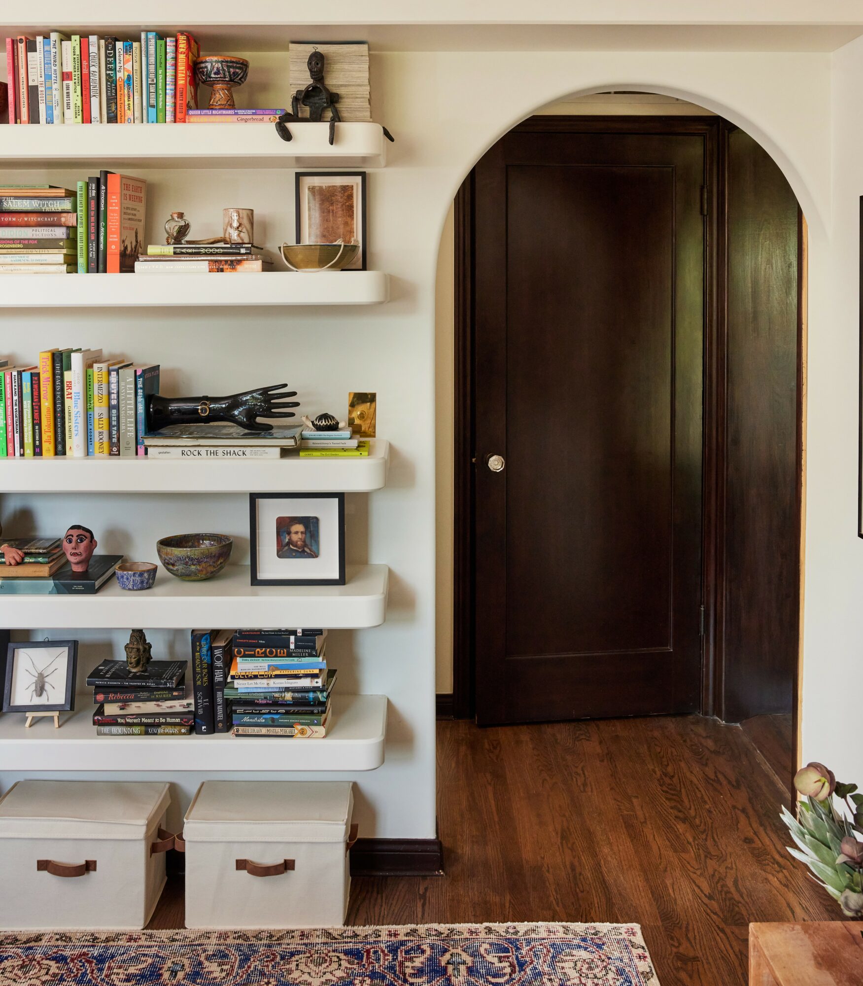 Bookshelves filled with books and decorative items, dark wooden door, hardwood floor, and a patterned rug in a room.