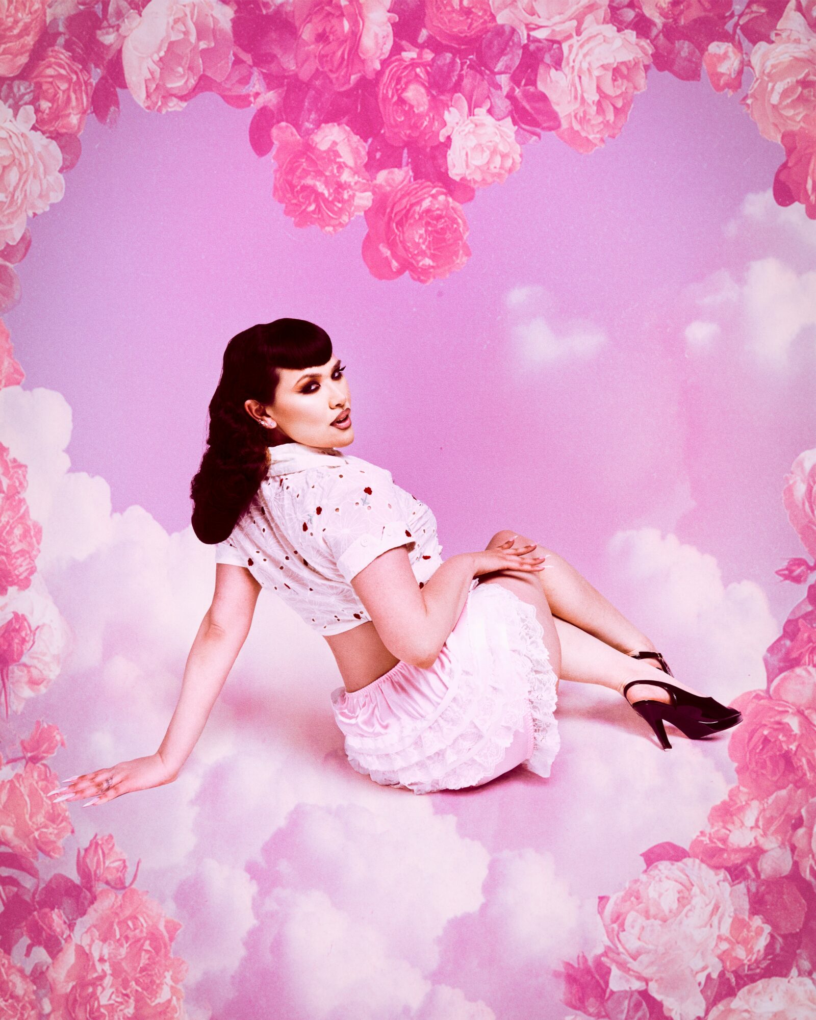 Woman in vintage clothing sitting on pink clouds surrounded by pink flowers, with a pink sky background.
