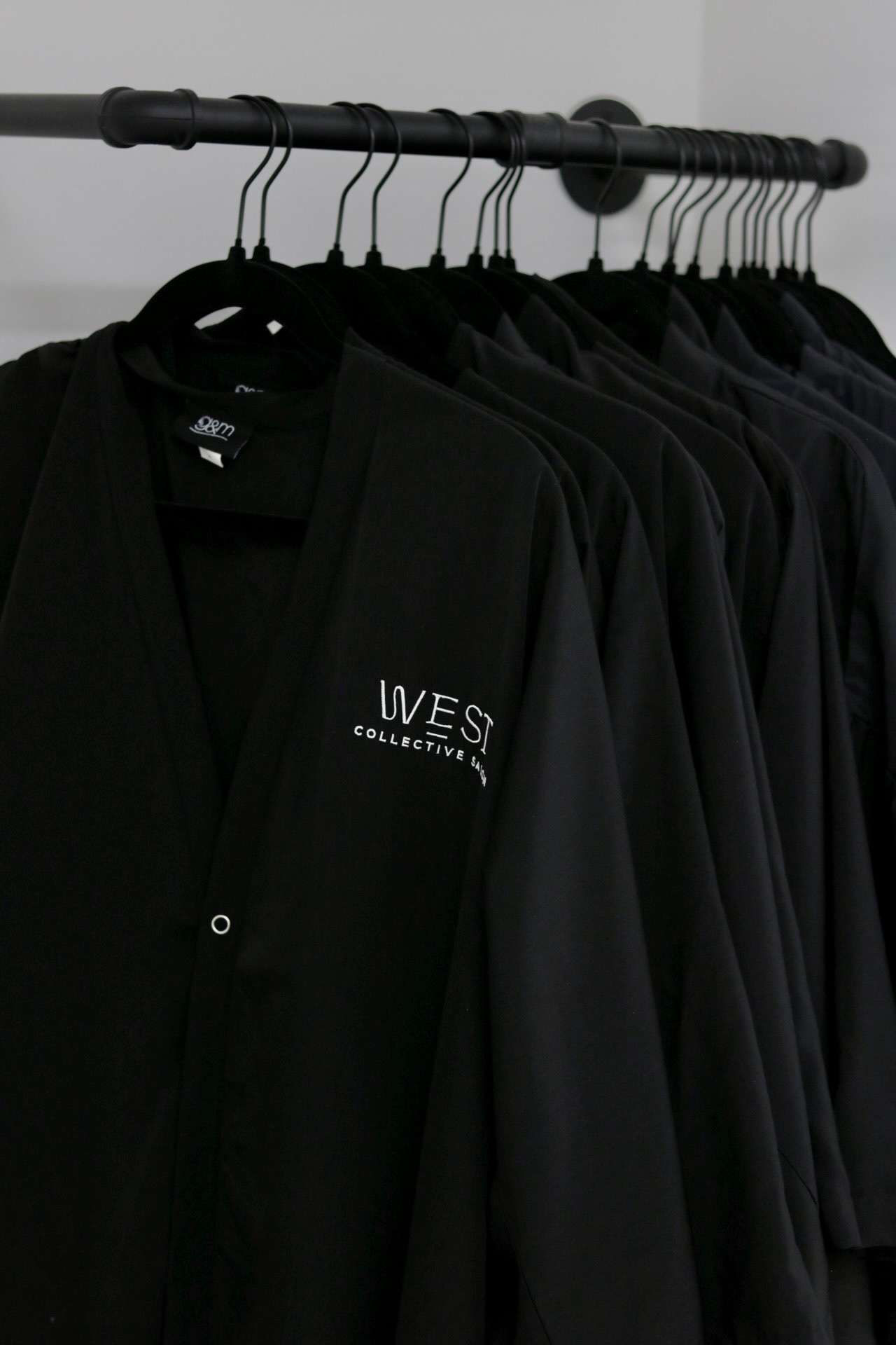 Black jackets hanging on a metal rod, with a label reading 'WES COLLECTION' visible on one jacket.
