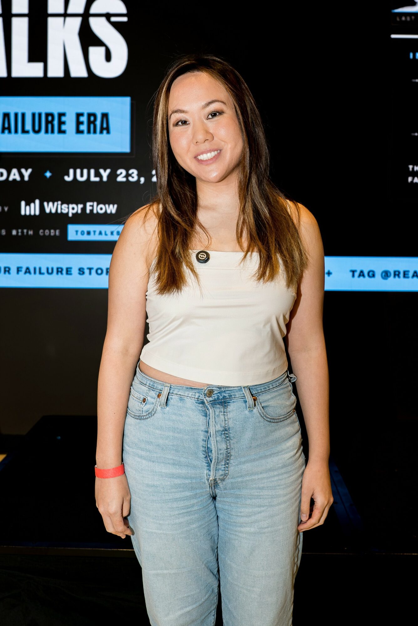 Young woman with long hair smiling, wearing a white top and light blue jeans, standing in front of a black background with blue text.