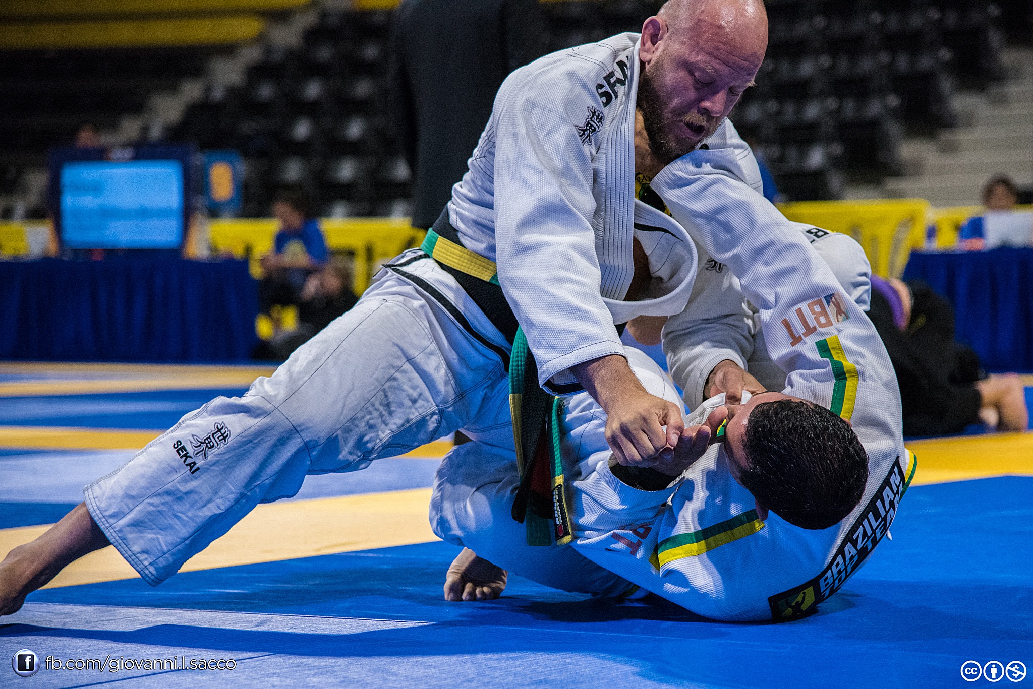 Two people practicing Brazilian Jiu-Jitsu on a mat, one applying a submission hold on the other, in a competition setting.