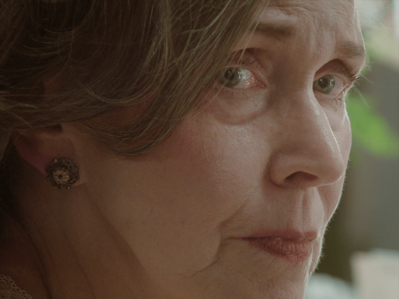 Close-up of a woman's face with light-colored eyes and earrings, looking to the side.