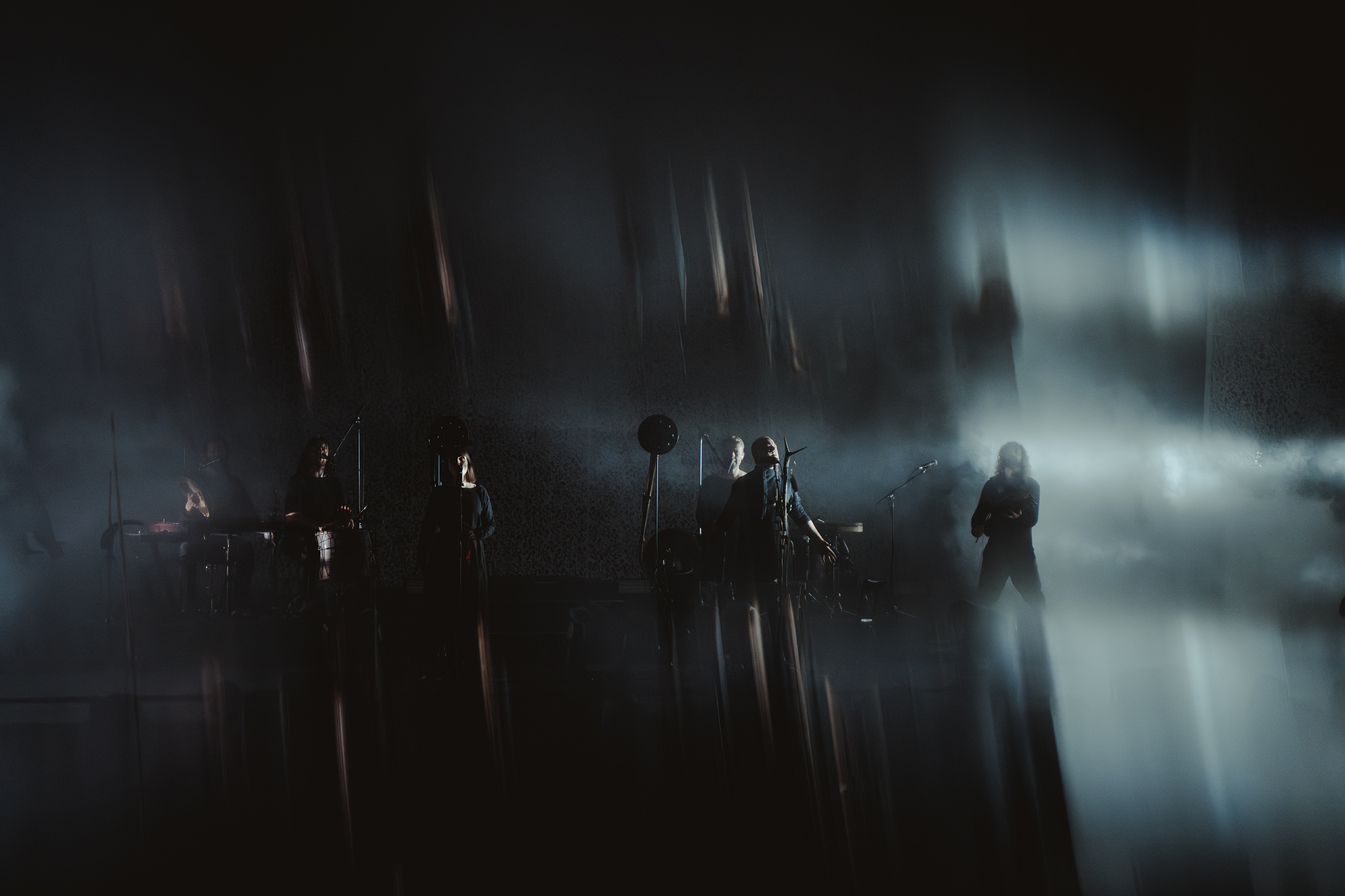 Dark scene with silhouettes of people and bright light beams, creating a mysterious atmosphere.