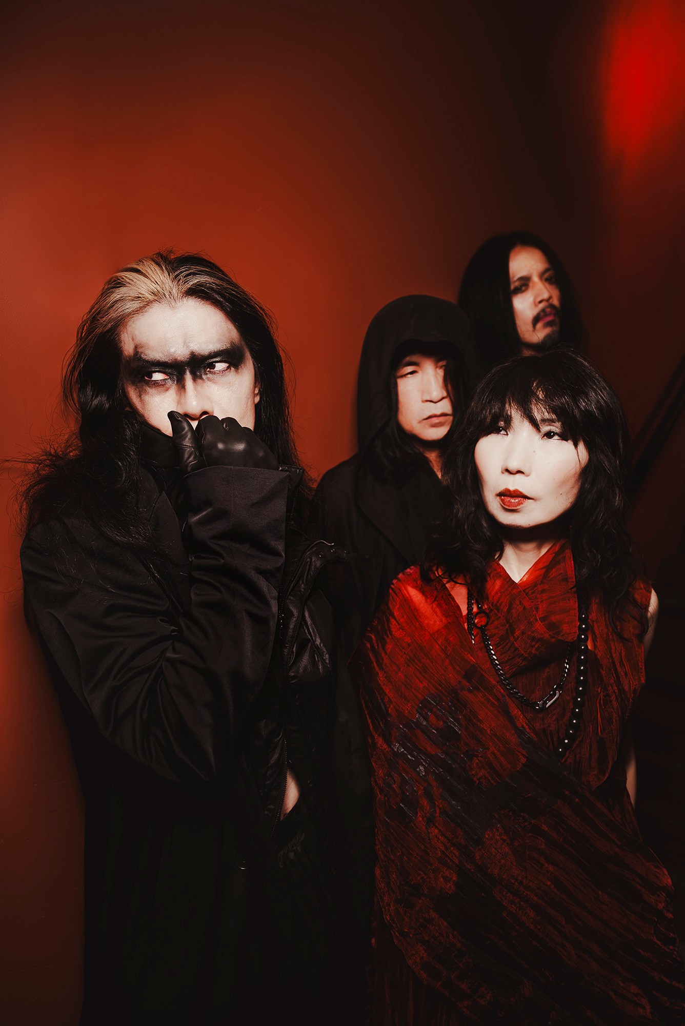 Four people with dark clothing and makeup pose against a red and black background.