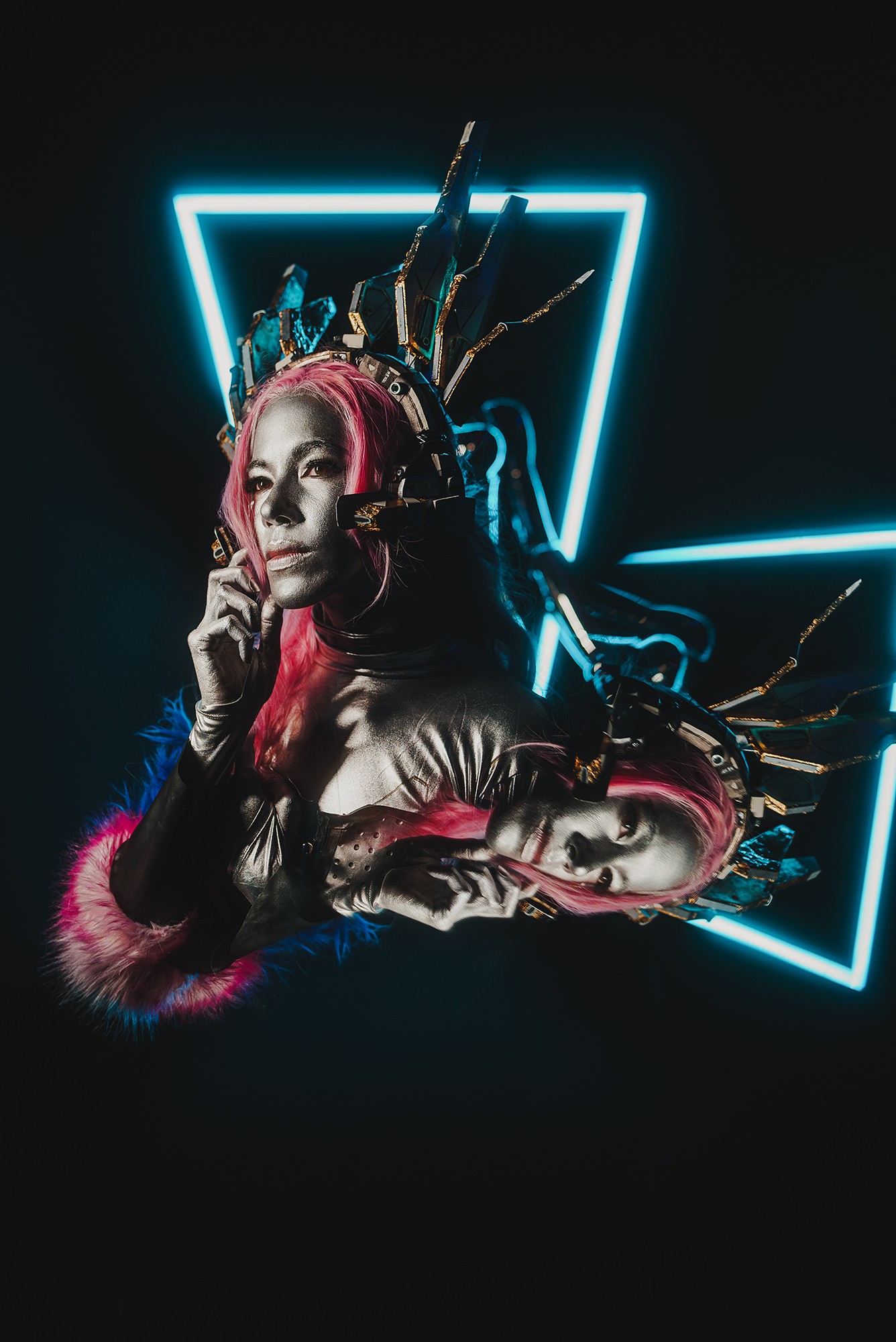 Woman with pink hair and elaborate headpiece poses in front of neon geometric shapes, holding her chin with one hand.