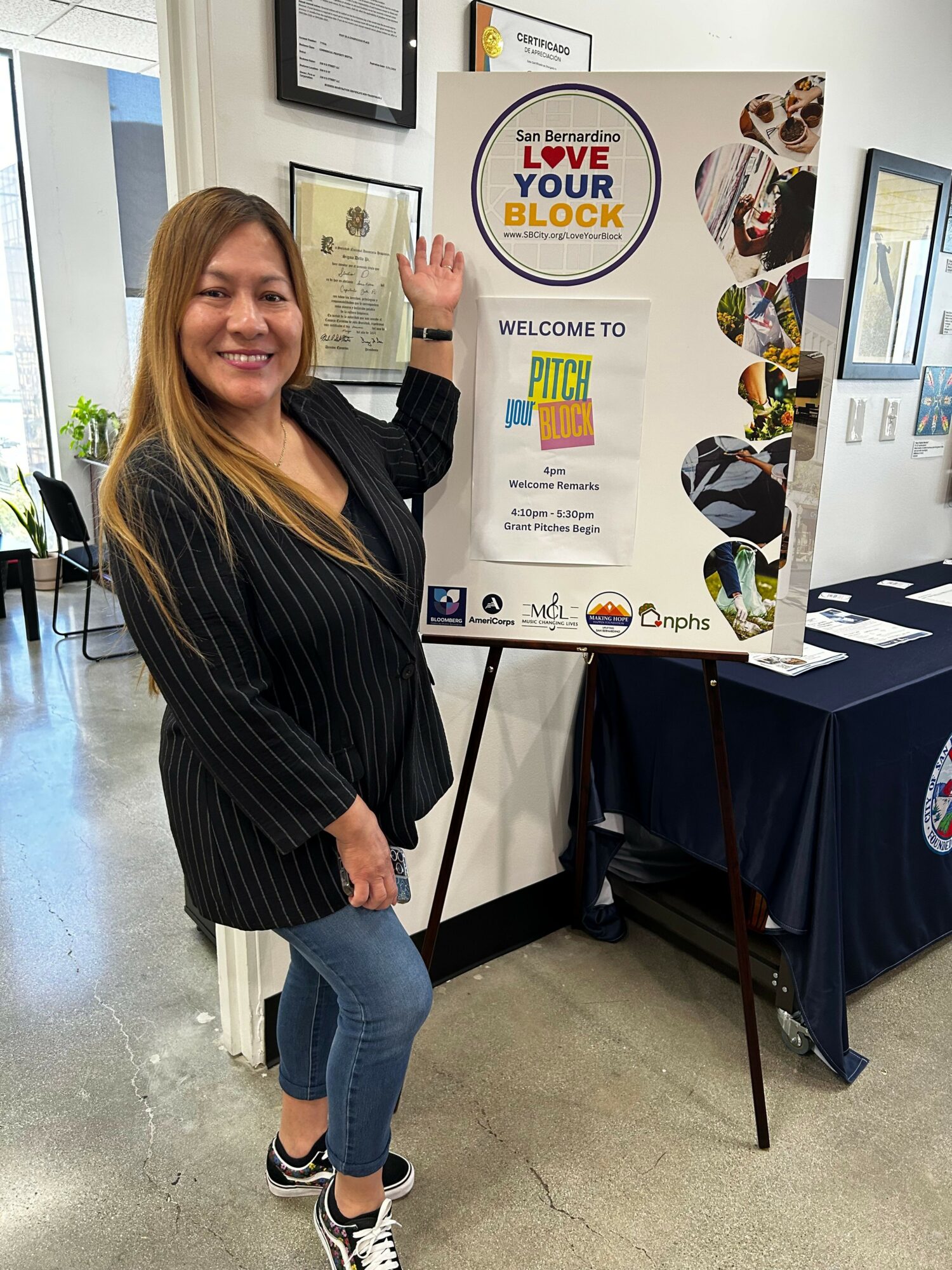 Woman standing next to a colorful informational poster on a table, smiling, in an indoor setting.