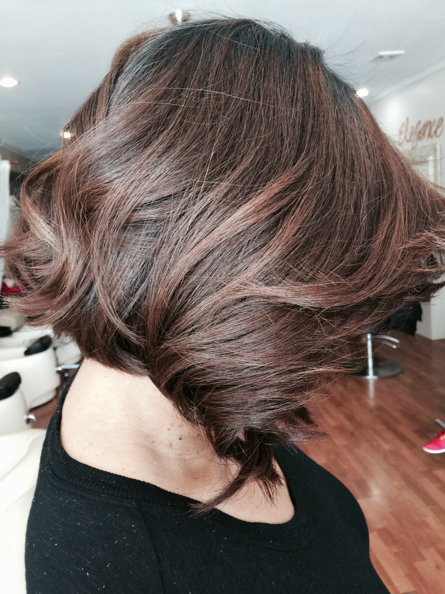 Side view of a woman with a short, layered, reddish-brown hairstyle in a salon.