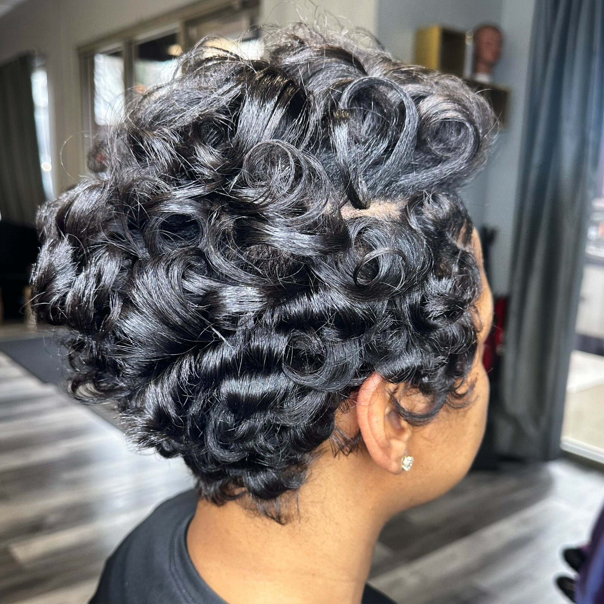 Close-up of a woman's curly, styled hair with a short haircut, indoors with a blurred background.