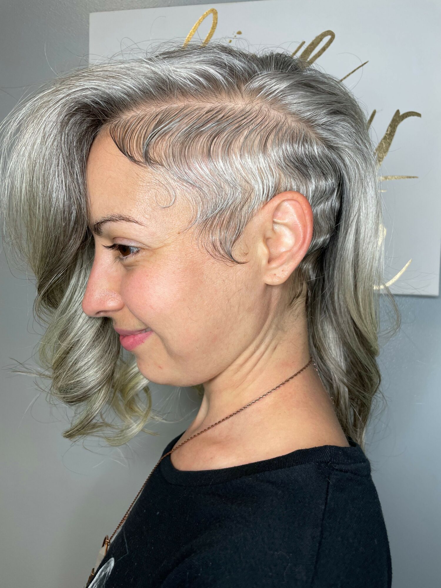 Side profile of a woman with gray hair, looking downward, wearing a black top, in a well-lit room.