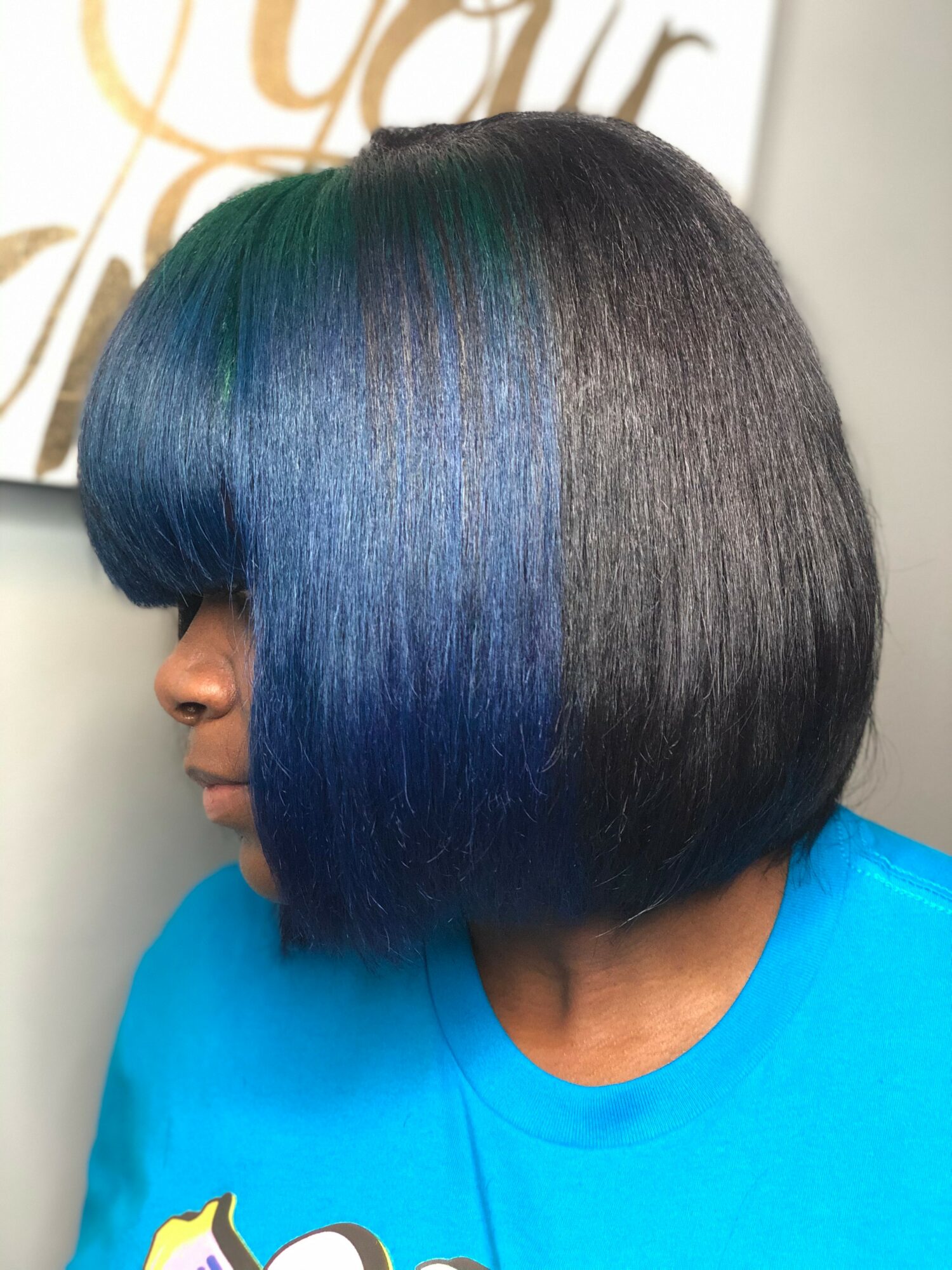 Side view of a woman with a short, straight bob hairstyle dyed blue and black, wearing a blue shirt.