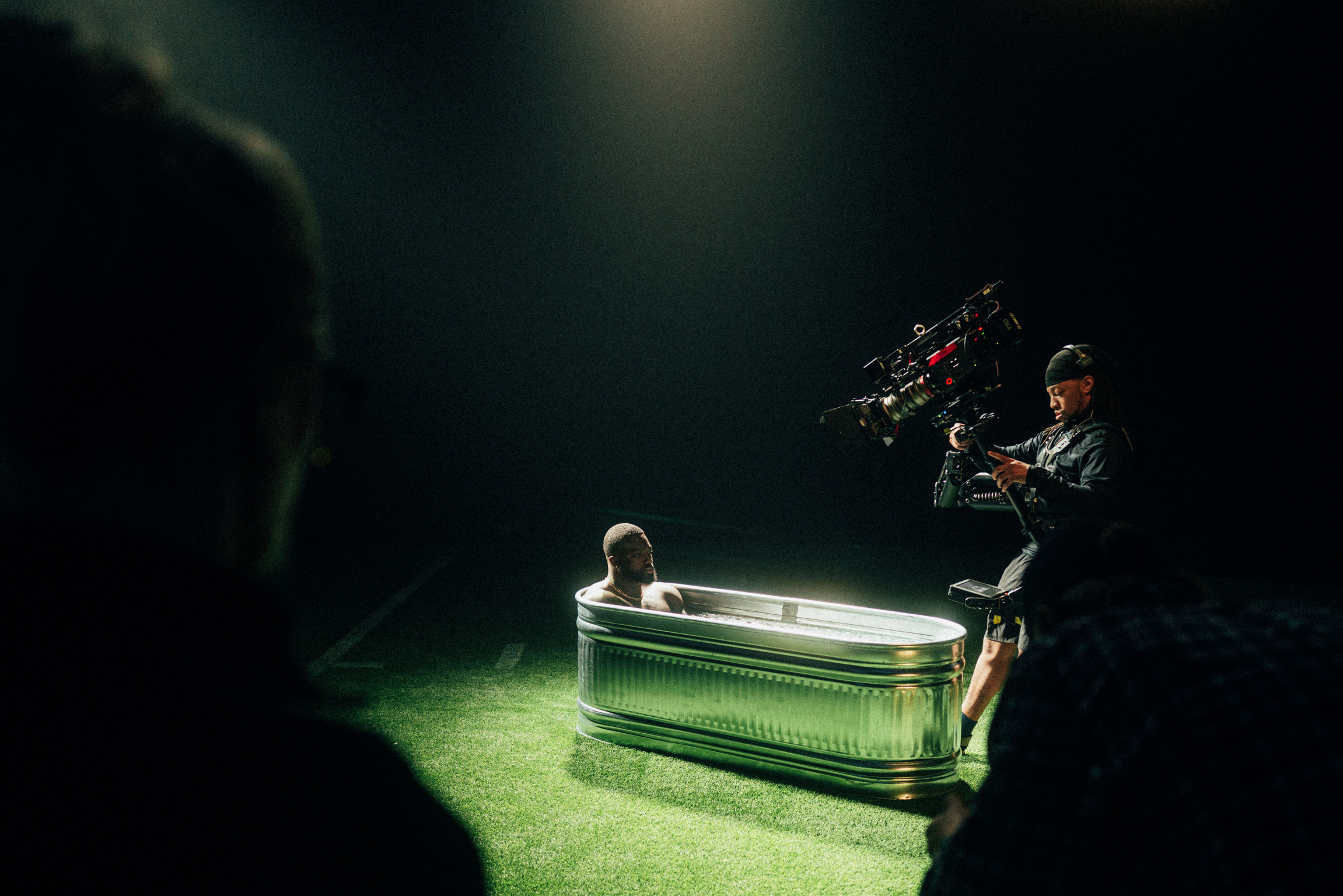 Person playing a green piano on stage with a camera operator nearby, in a dark setting with spotlighting.