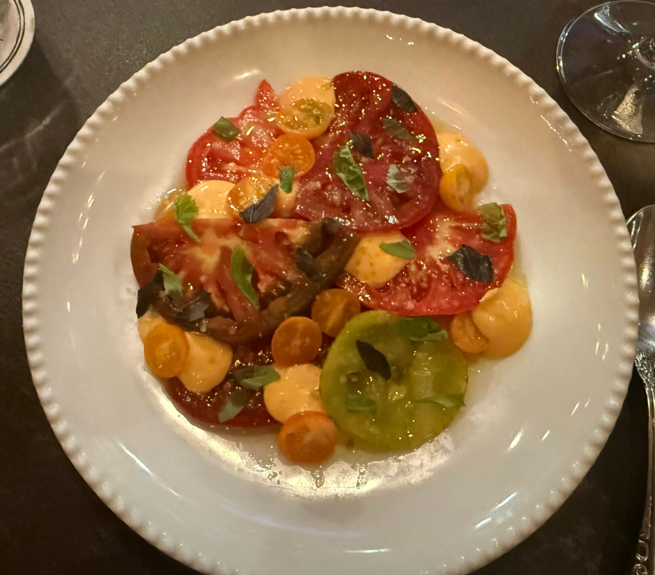 Plate with sliced tomatoes, green and yellow vegetables, garnished with herbs, on a white dish.