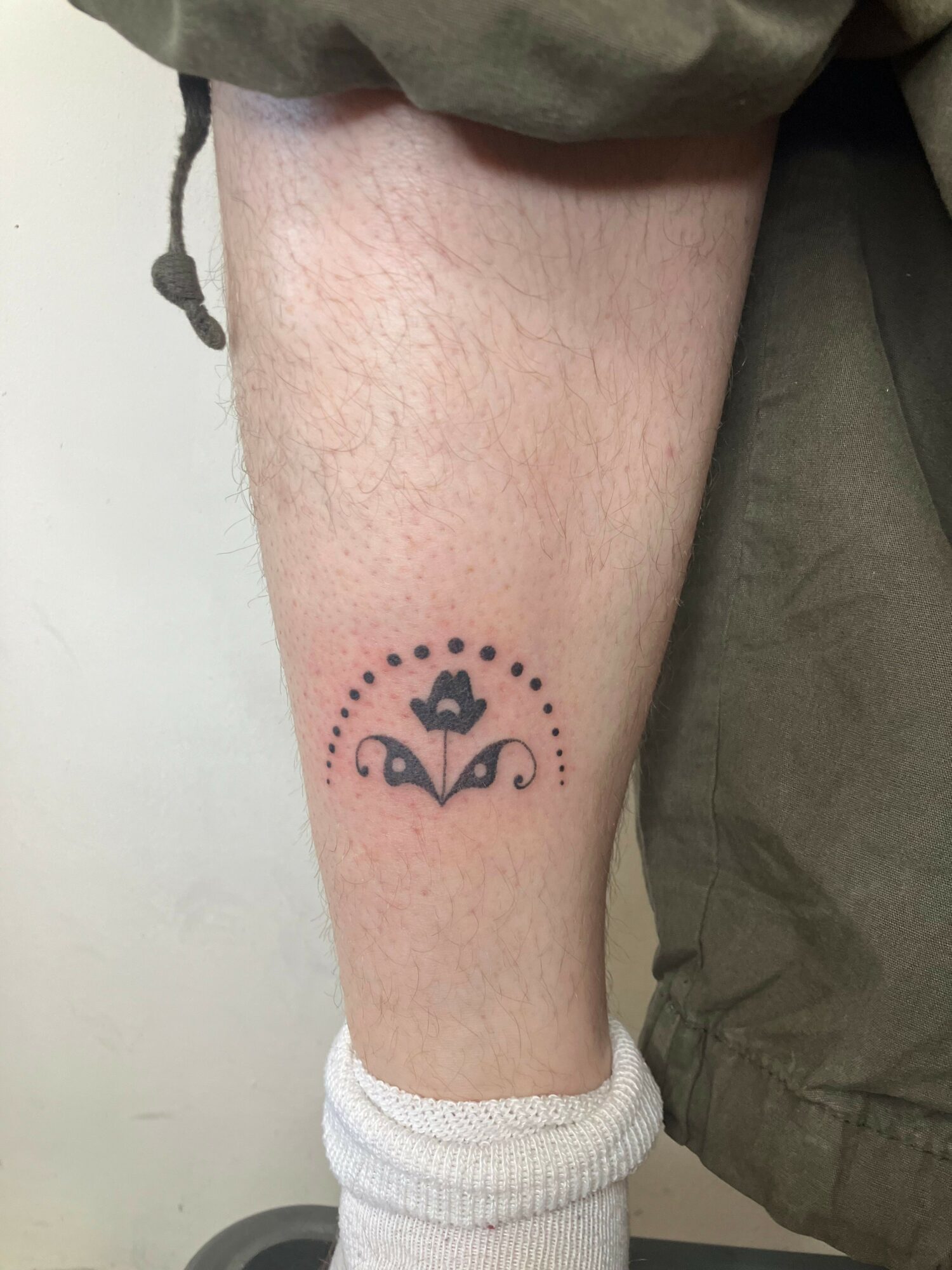 Tattoo of a crown with dots around it on person's ankle, with a sock partially covering the leg.
