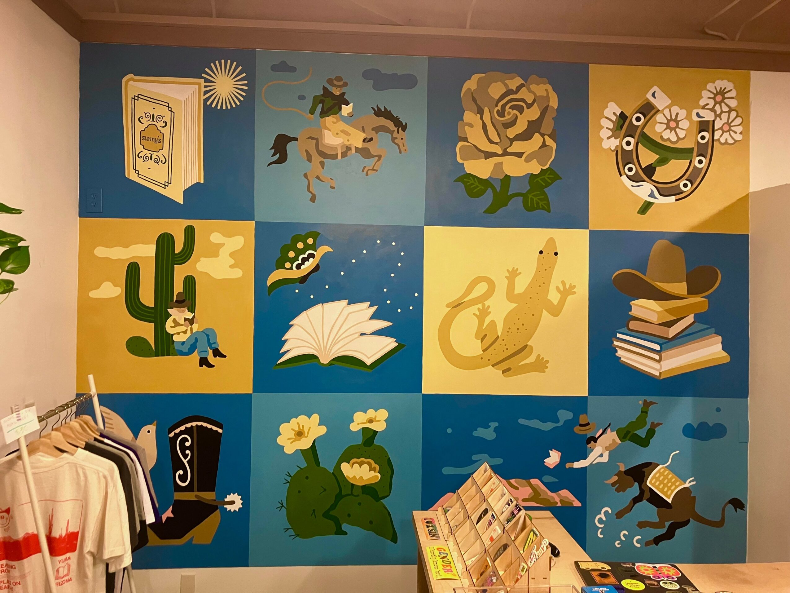 Colorful mural with animals, plants, books, and abstract designs on a wall, with clothing hanging in front.
