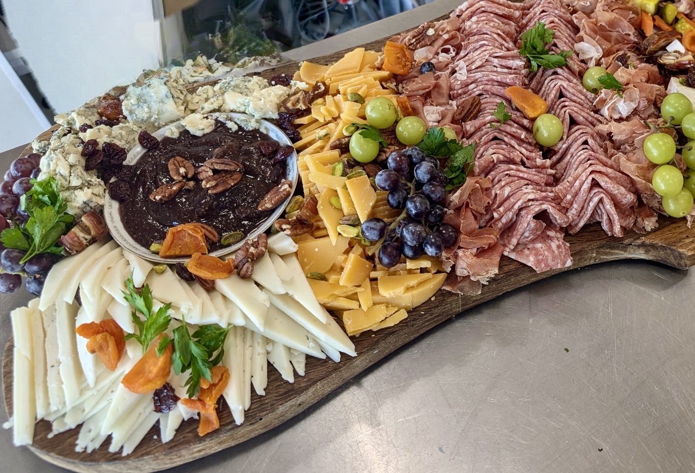 Assorted cheeses, grapes, sliced meats, and a bowl of dark spread on a wooden platter.