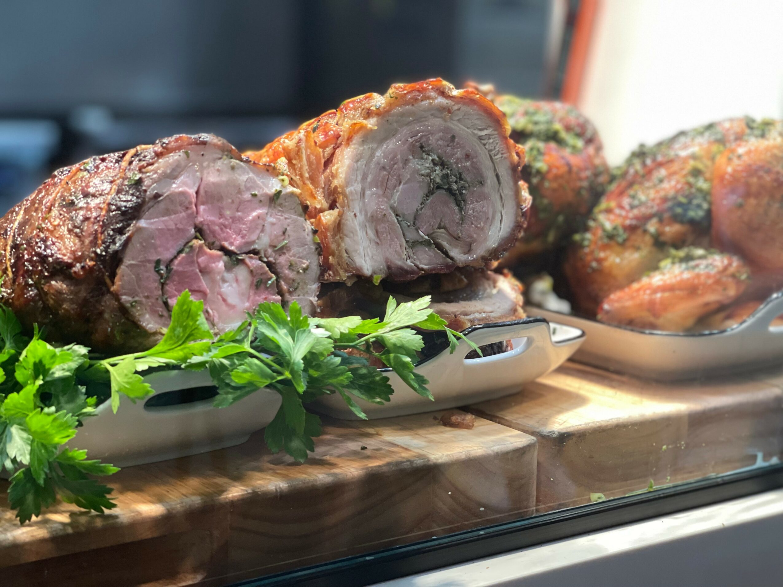 Roast beef with a pink center on a white plate, garnished with green herbs, on a wooden surface.
