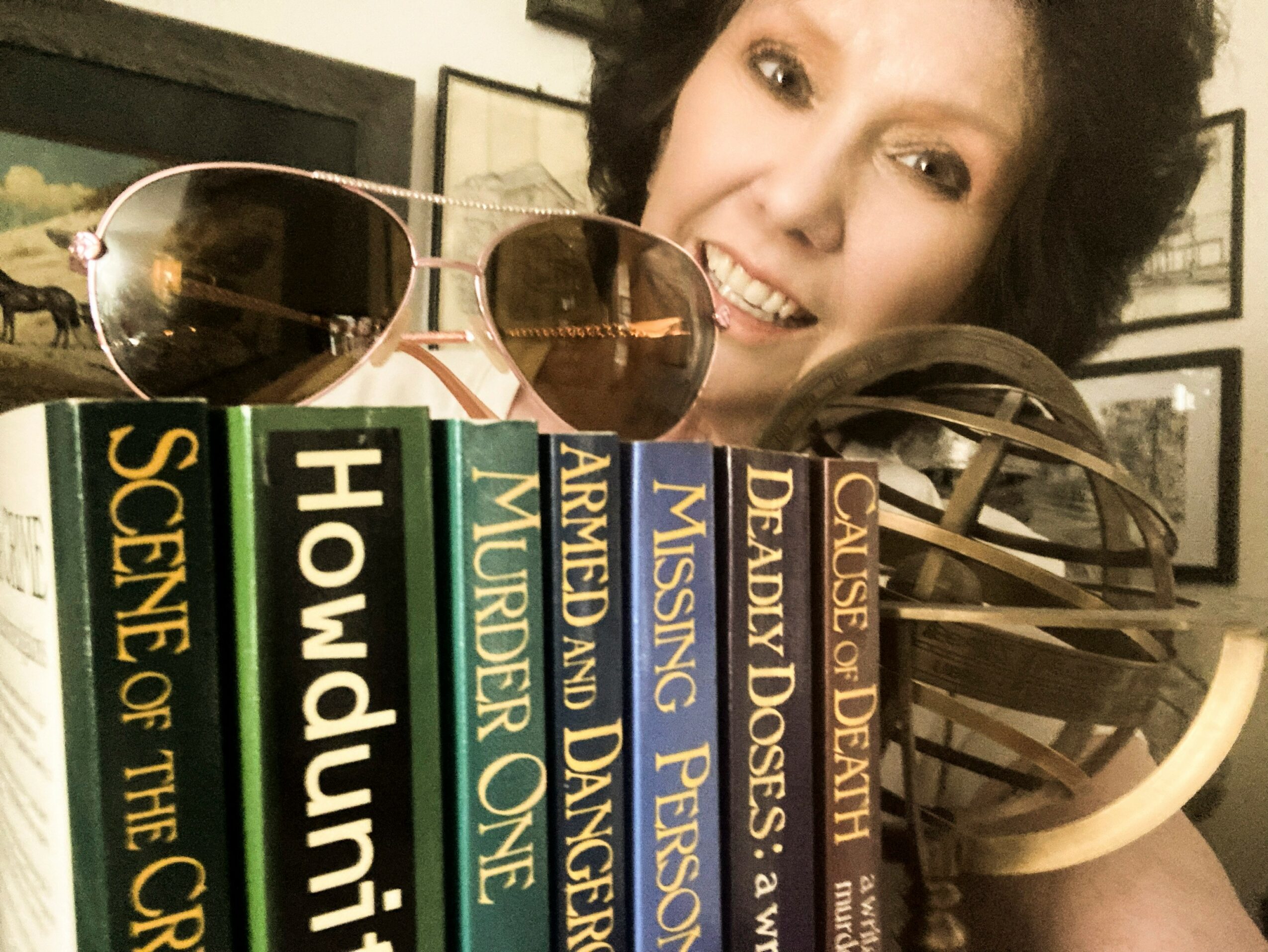 Person with curly hair smiling behind sunglasses and a striped bag, with framed pictures on the wall in the background.