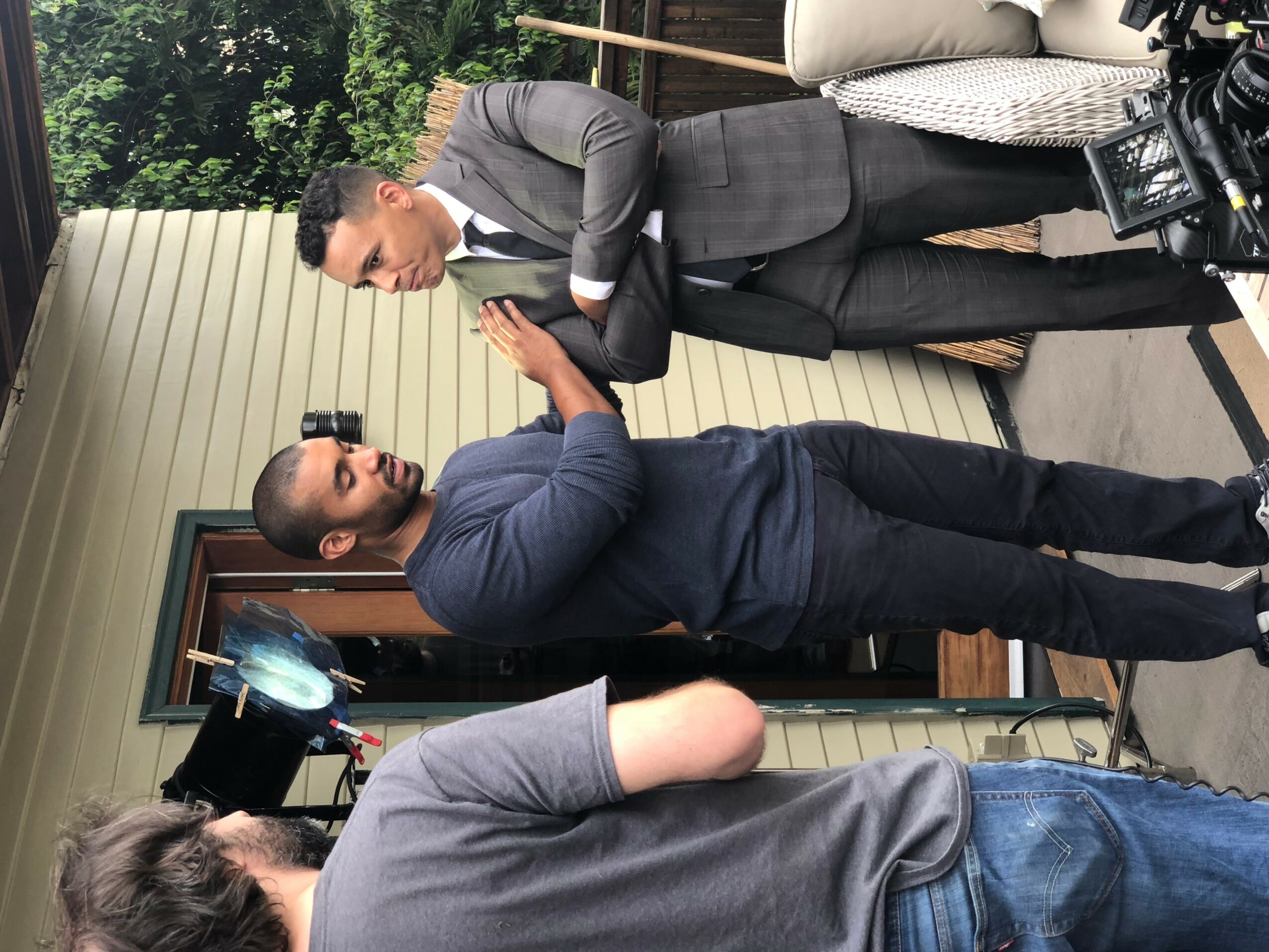 Two men in suits greeting each other with a handshake outdoors, with a woman in a gray shirt nearby.