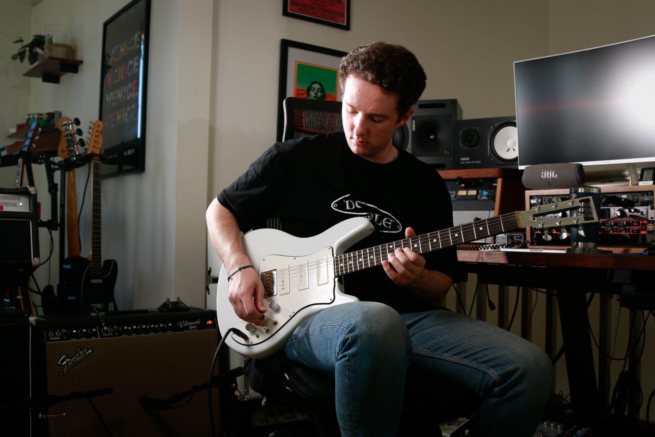 Person playing white electric guitar in a music studio with monitors and equipment