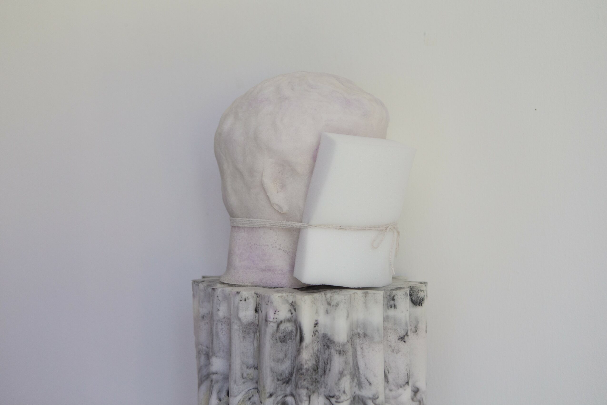 White bust sculpture on a textured pedestal with a plain background.