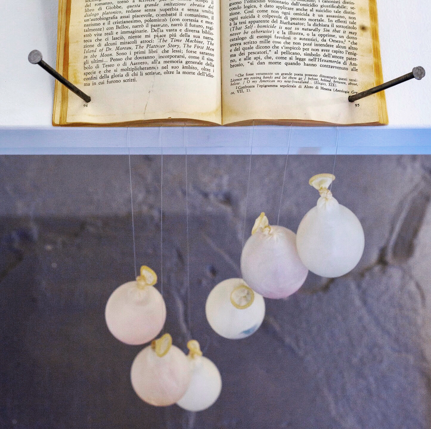 Open book on a stand with hanging white balloons below, against a stone wall background.