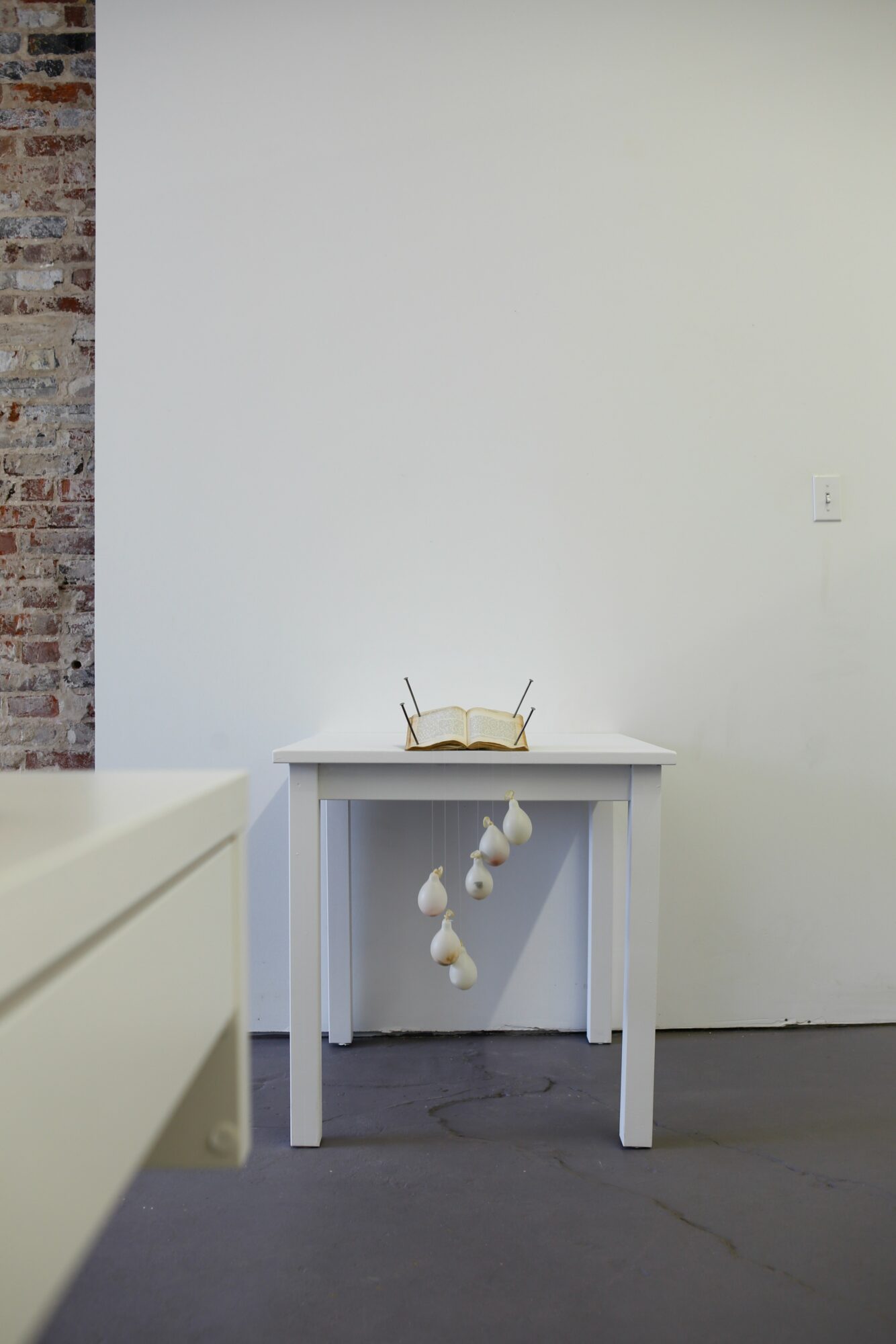 Small table with hanging white flowers against a plain white wall and brick wall, minimalistic setting.