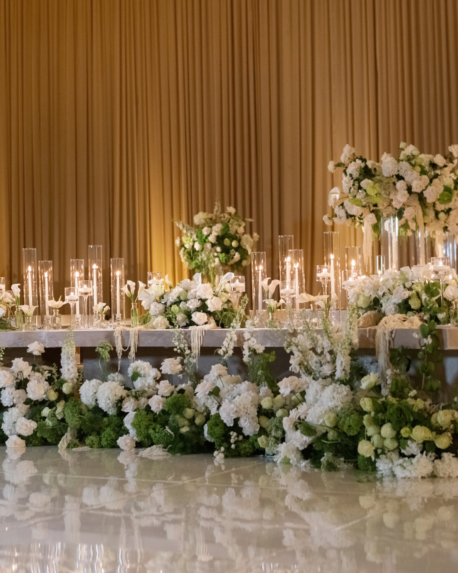 Elegant table decorated with white flowers and candles, with a gold curtain backdrop.