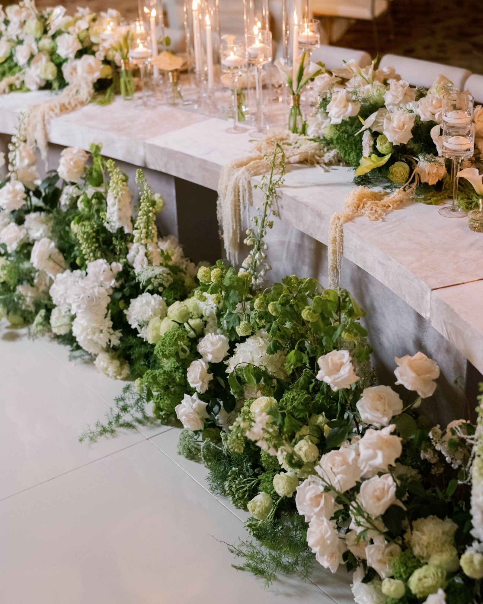 Elegant table decorated with white and green flowers, candles, and glassware for a celebration or wedding.
