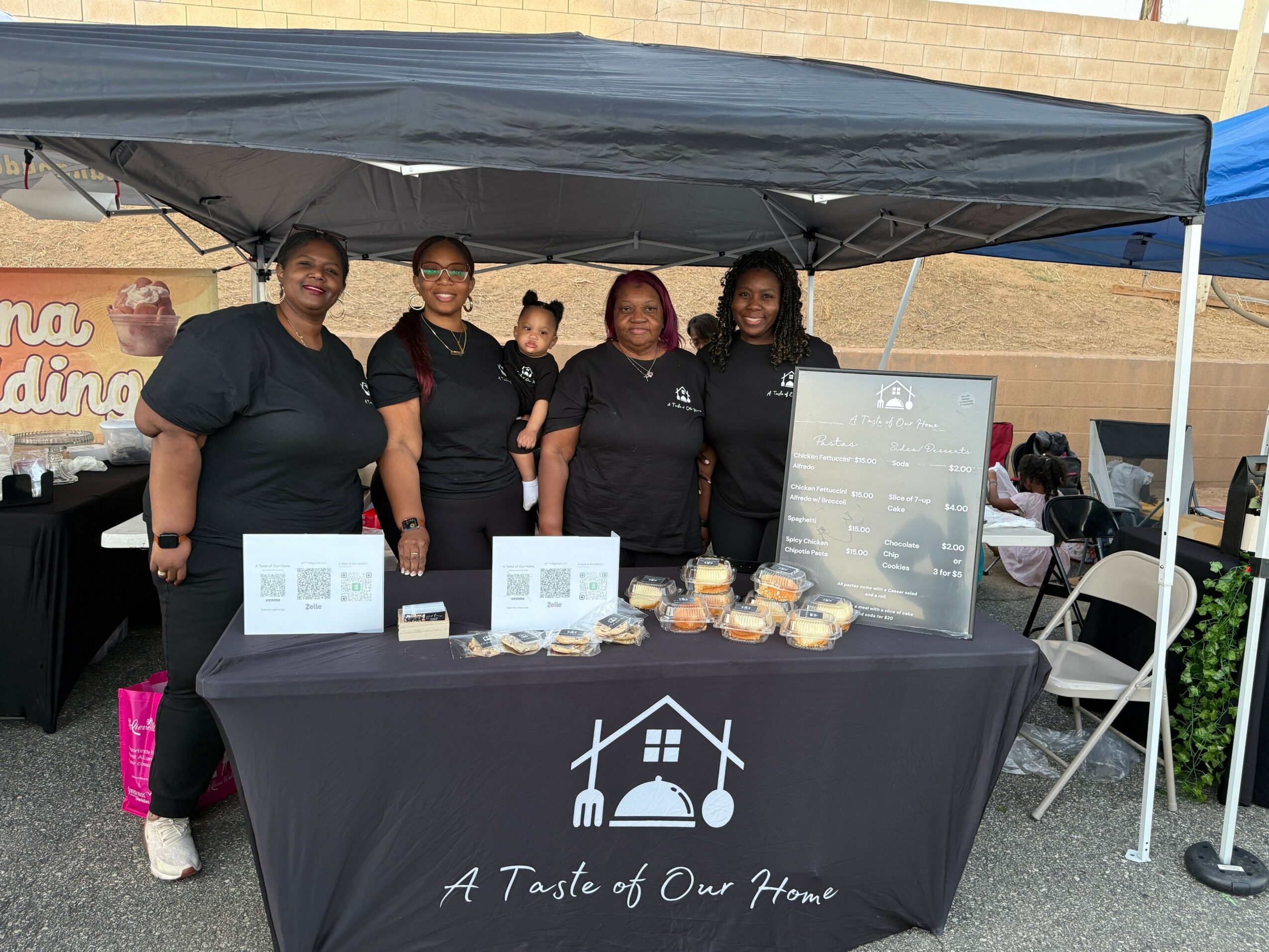 Four people standing behind a table with food, under a black canopy with white text and graphics, upside down.