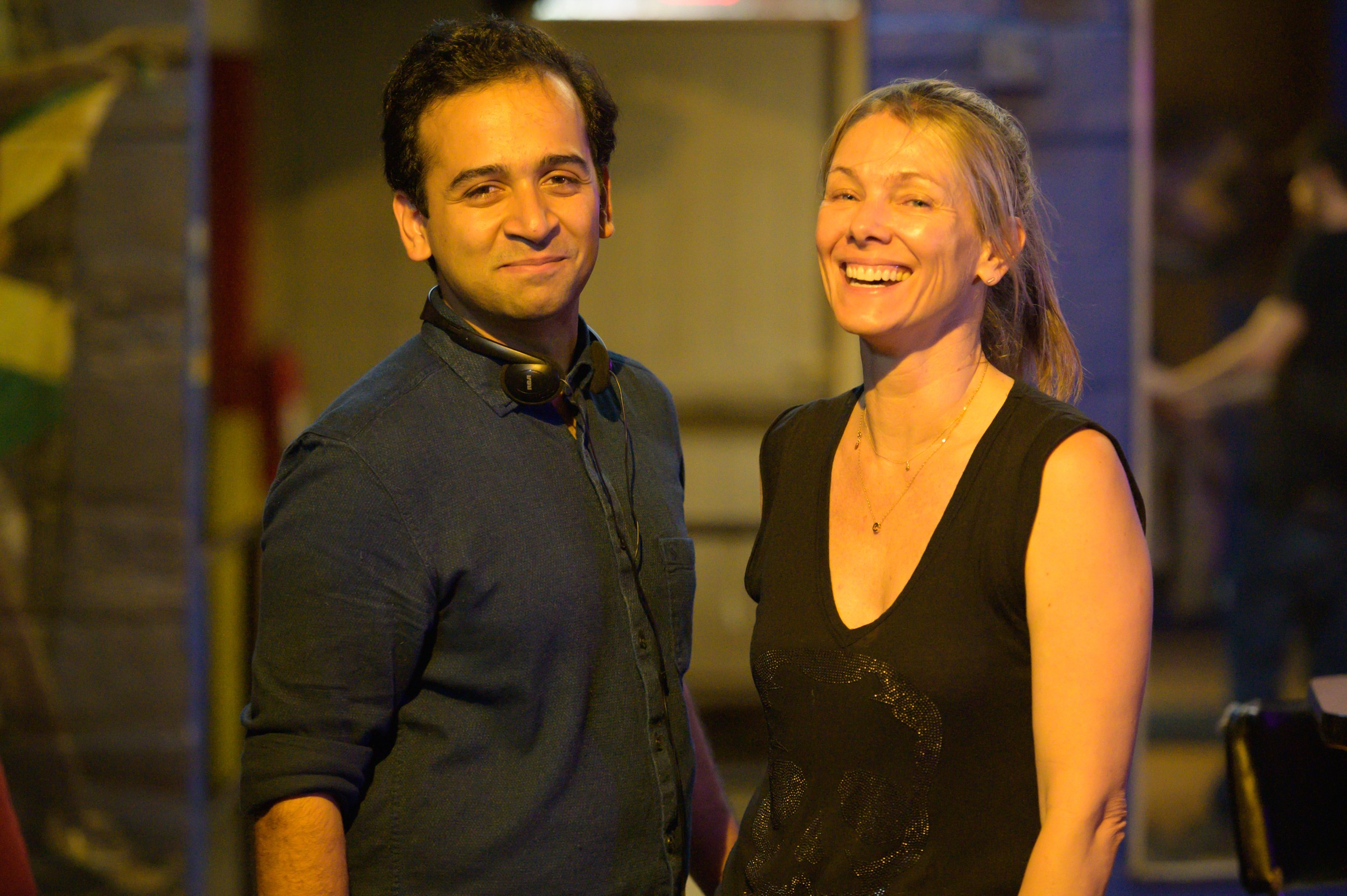 A man and woman smiling together at an indoor event, with warm lighting and blurred background.